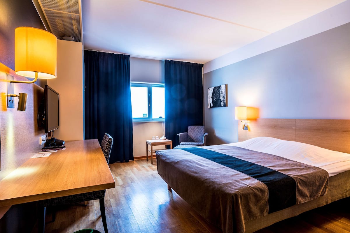 A hotel room with a bed, a desk, a chair, a TV, and a window with curtains.