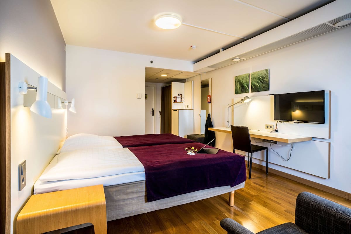 A modern hotel room with a bed, desk, chair, and TV.