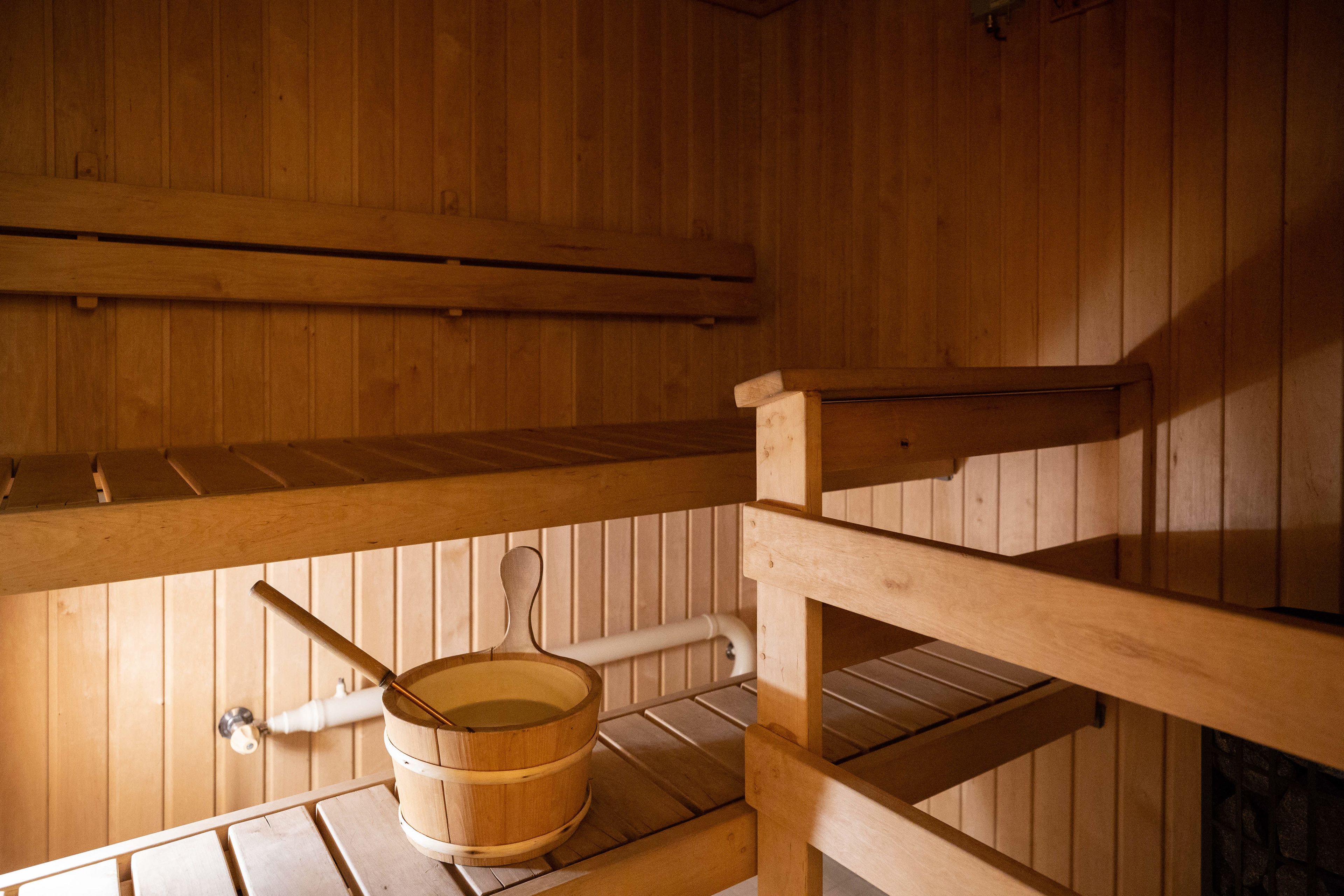 Una sauna de madera con un banco de madera, un cubo y una tubería.