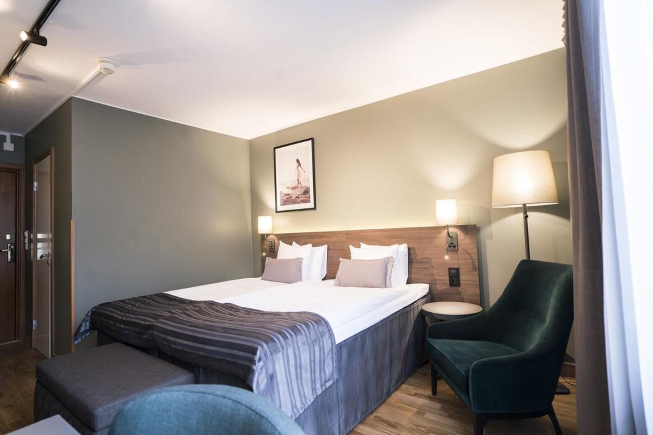 Une chambre d’hôtel avec un lit, une table de chevet, une chaise et un tableau au mur.