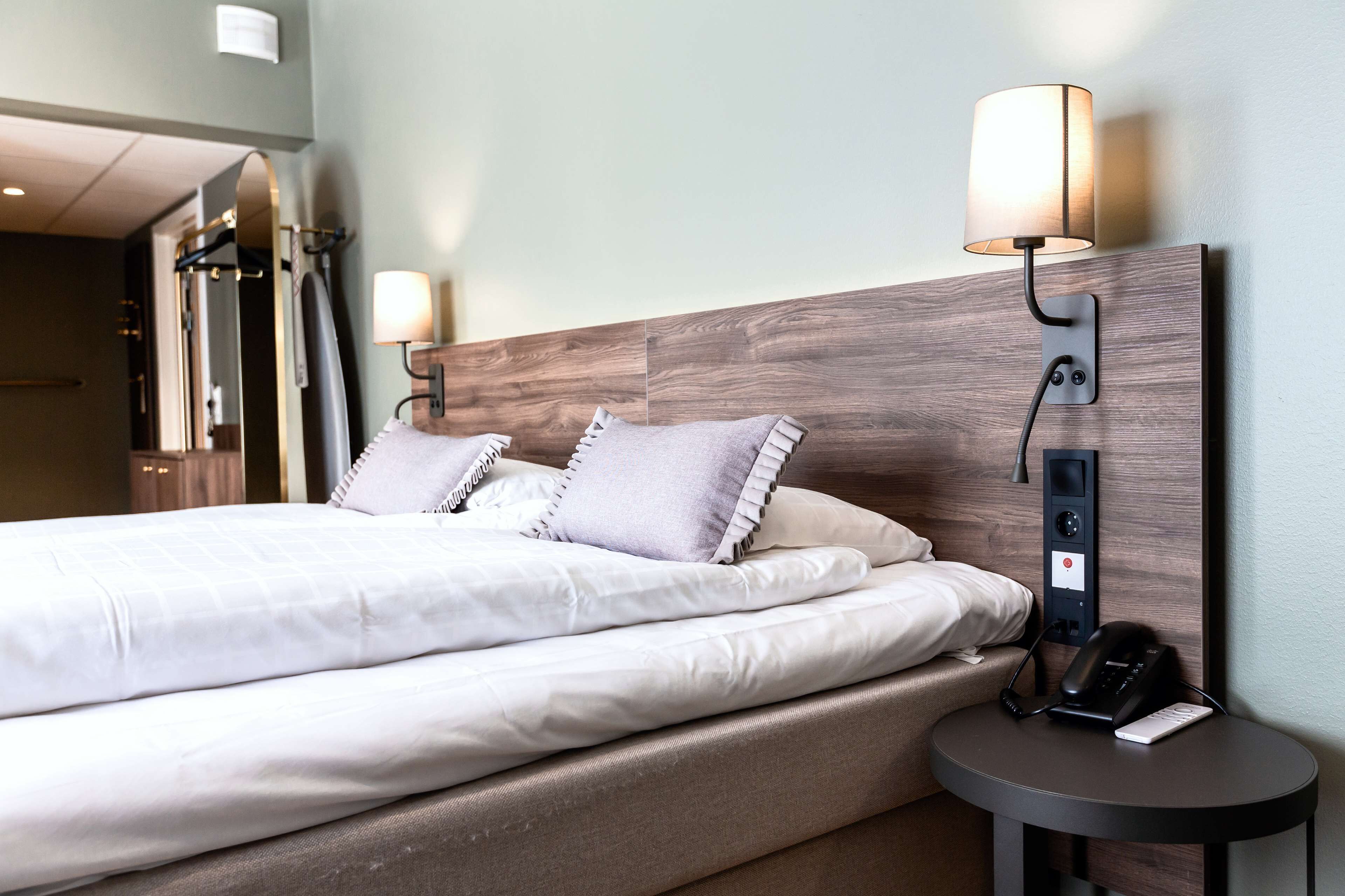 A neatly made bed with pillows, a bedside table with a lamp, and a phone.
