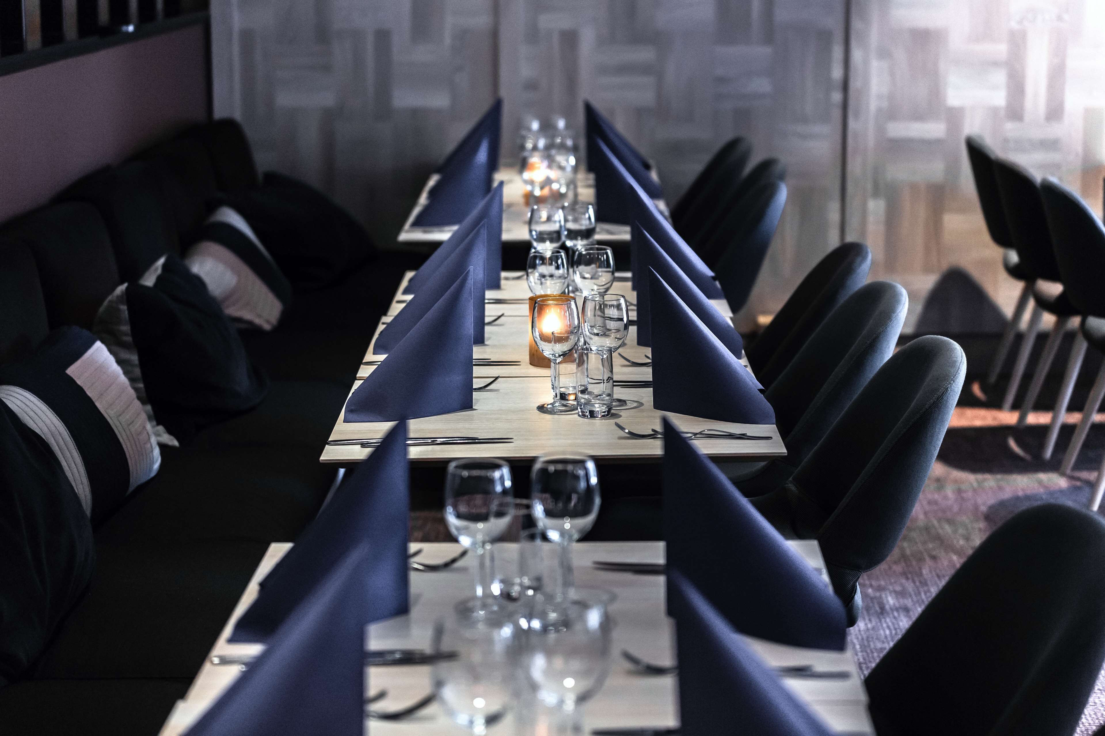 A long dining table set with blue napkins, glasses, and a candle.