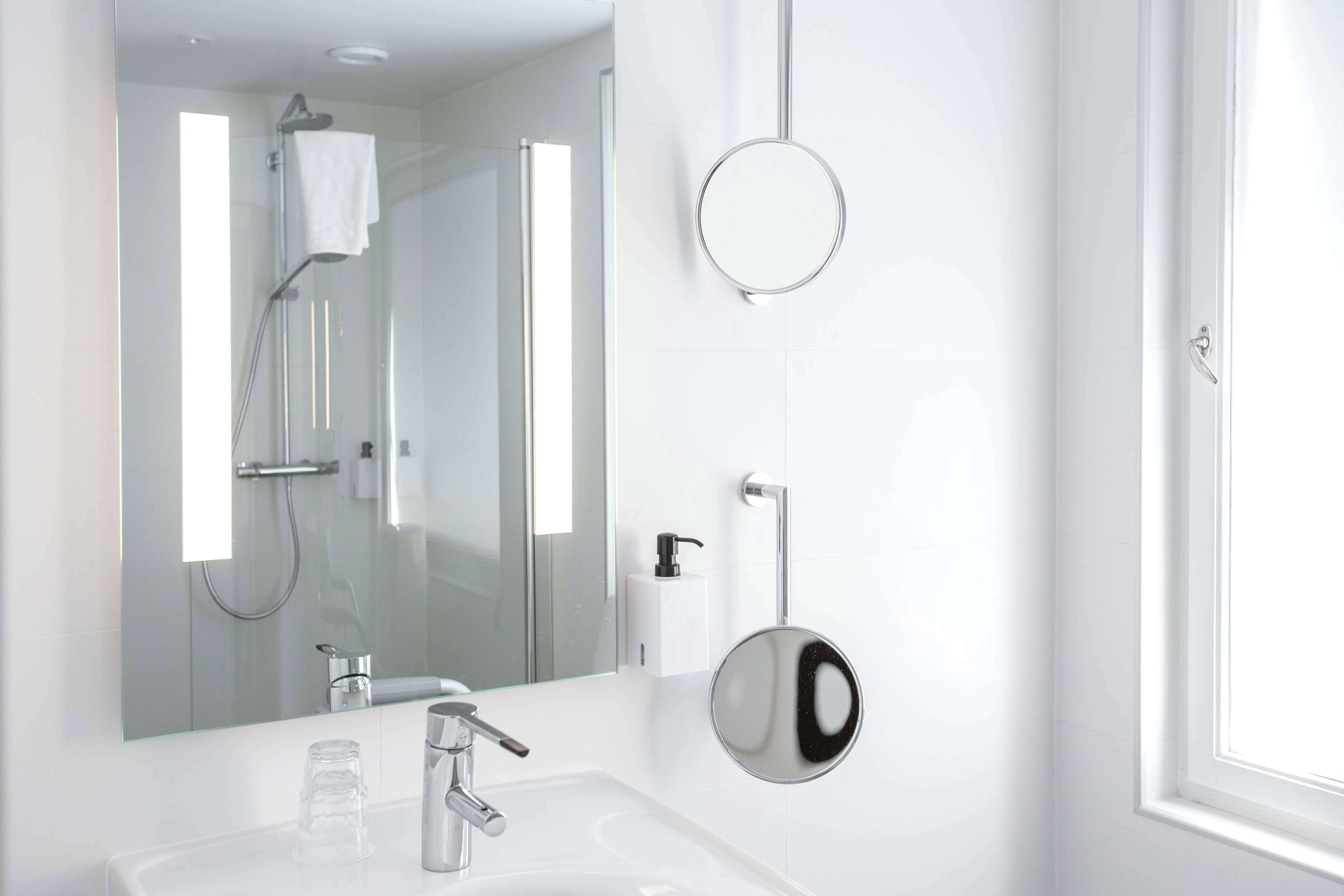 A modern bathroom with a large mirror, a handheld showerhead, and a wall-mounted soap dispenser.