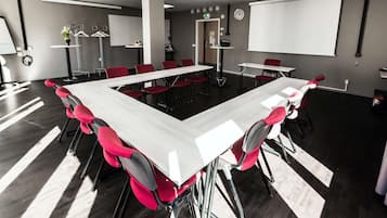 Un salón de conferencias con una larga mesa, sillas rojas, una pantalla de proyector y una pizarra.