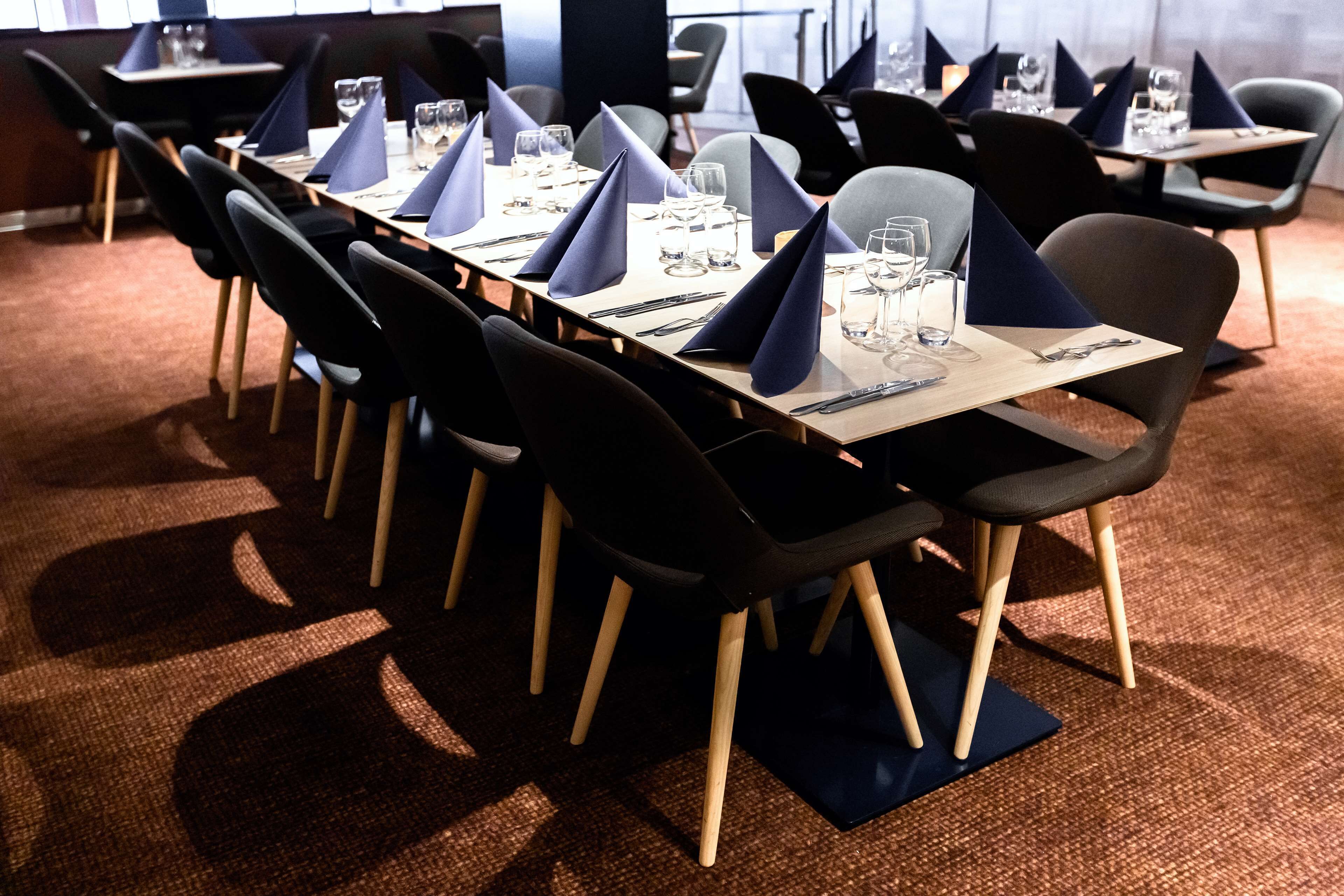 Un salón de conferencias con una larga mesa dispuesta para una reunión, equipado con sillas y mesas, y un piso alfombrado.