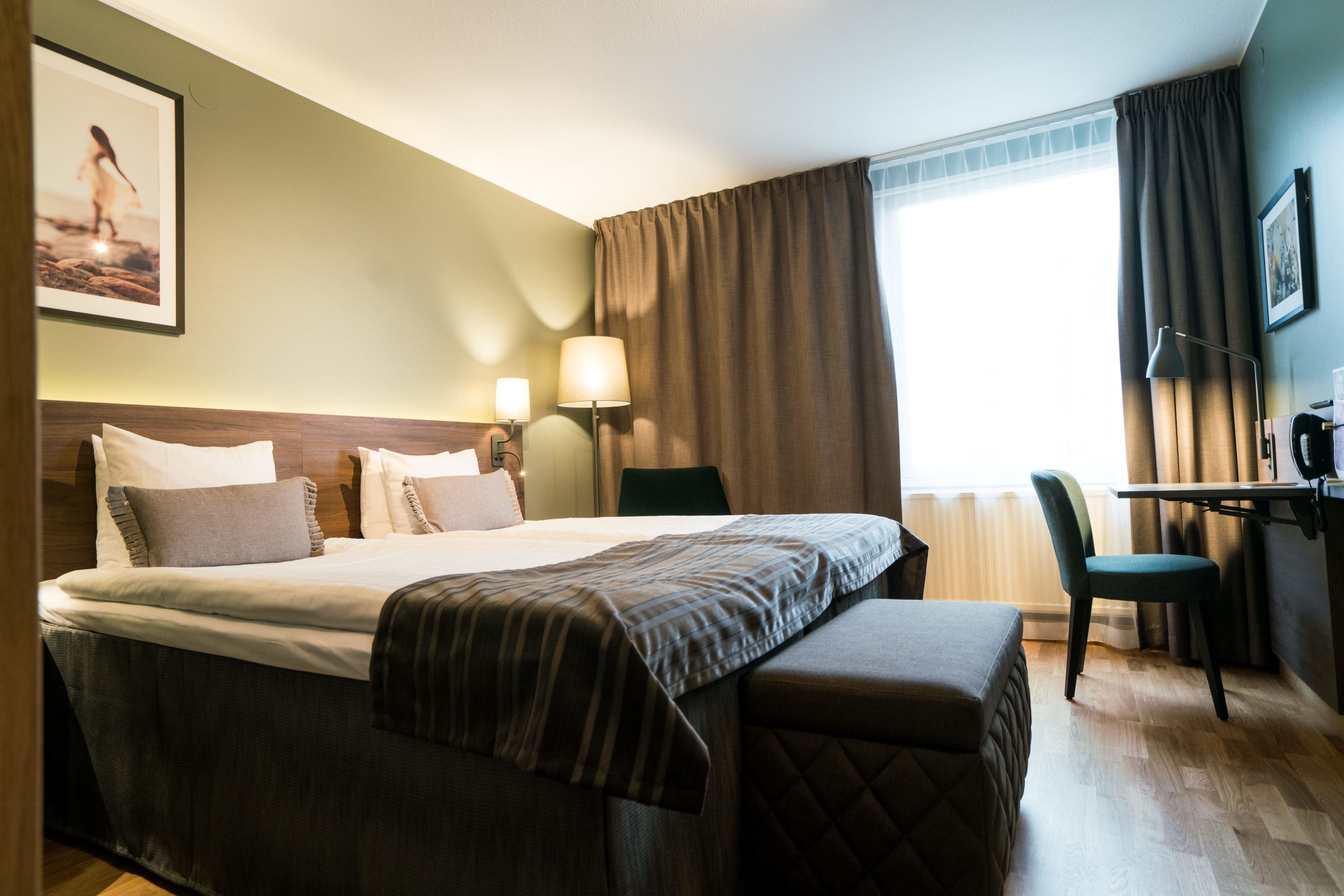 A hotel room with a large bed, a desk, a chair, and a window with curtains.