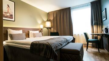 A hotel room with a large bed, a desk, a chair, and a window with curtains.