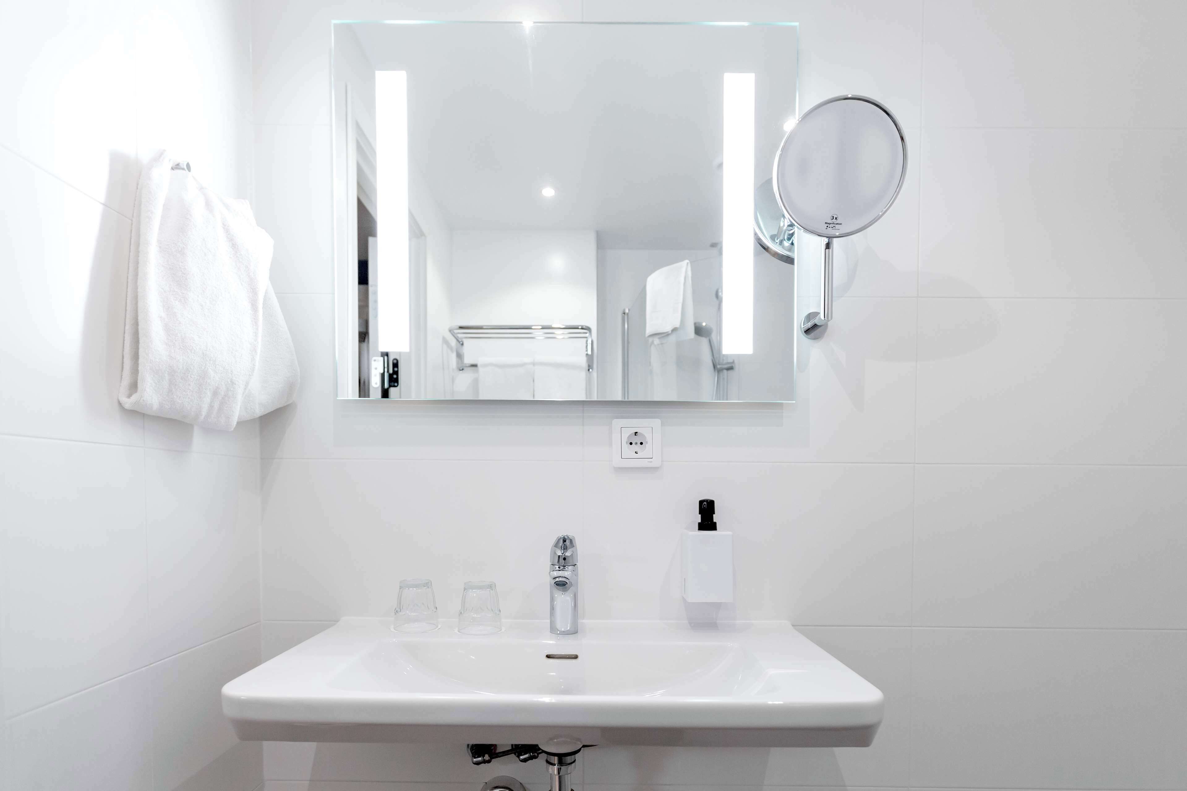 A modern bathroom with a white sink, a mirror, and a towel hanging on the wall.