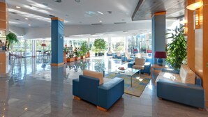 A spacious lobby with blue sofas, a glass coffee table, and potted plants. - Sol Port Cambrils (Cambrils)
