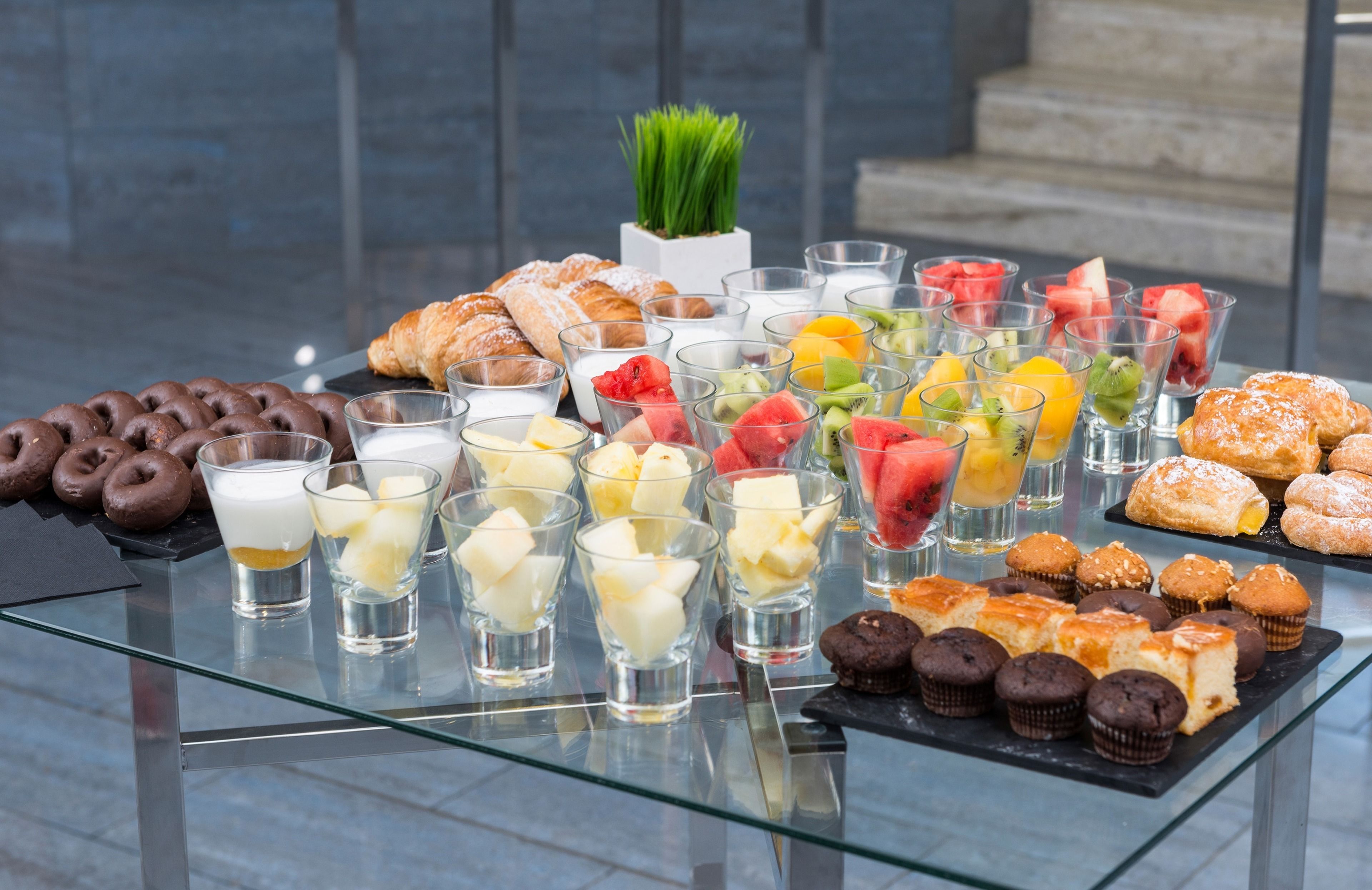A glass-topped table with various pastries, desserts, and fruit juices.