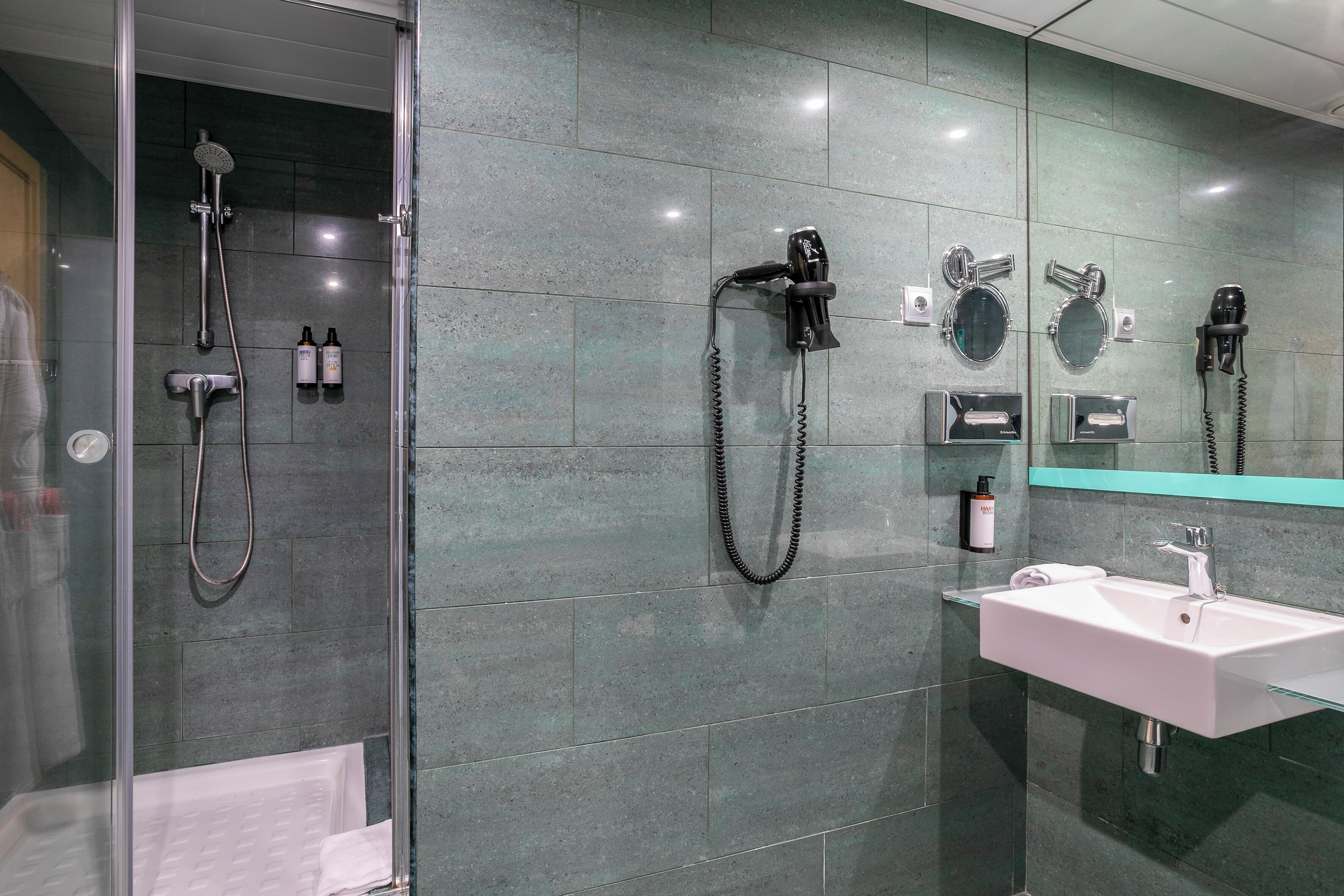 Une salle de bain moderne avec une douche à parois de verre, un lavabo avec un miroir et un sèche-cheveux fixé au mur.