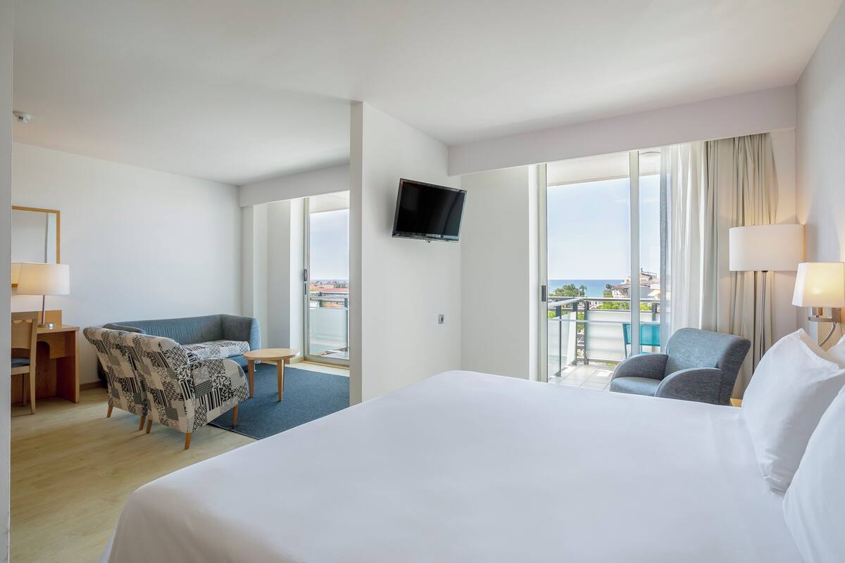 Une chambre d’hôtel avec un grand lit, un bureau avec une chaise, un canapé et un téléviseur fixé au mur.