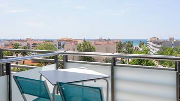 A balcony with a table and chairs, overlooking a coastal cityscape with buildings and a beach.