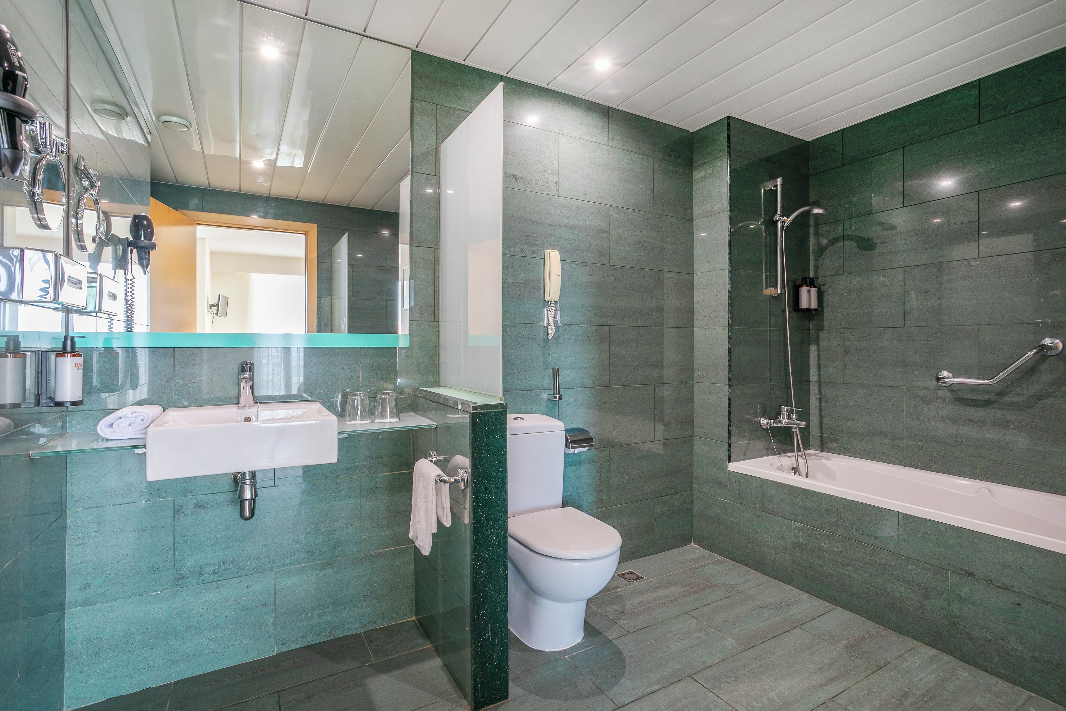Une salle de bain moderne avec un lavabo entouré de parois en verre, des toilettes et une douche à l’italienne.