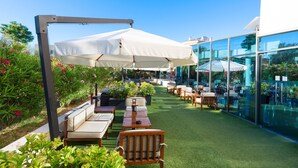 An outdoor patio area with seating arrangements, umbrellas, and a glass wall. - Sol Port Cambrils (Cambrils)