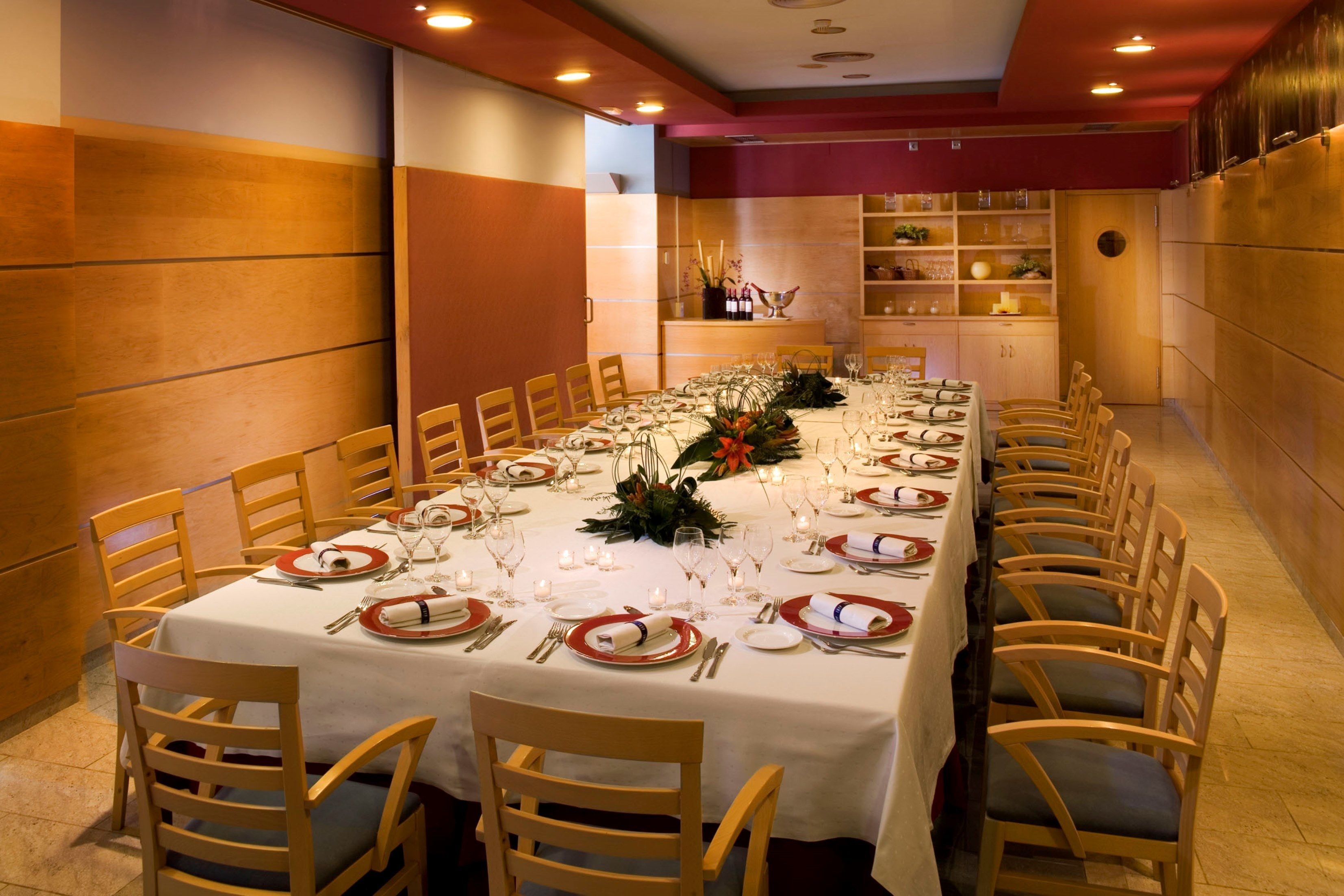 Una larga mesa de comedor dispuesta con sillas, manteles blancos y platos rojo y blanco.
