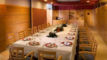 Una larga mesa de comedor dispuesta con sillas, manteles blancos y platos rojo y blanco.