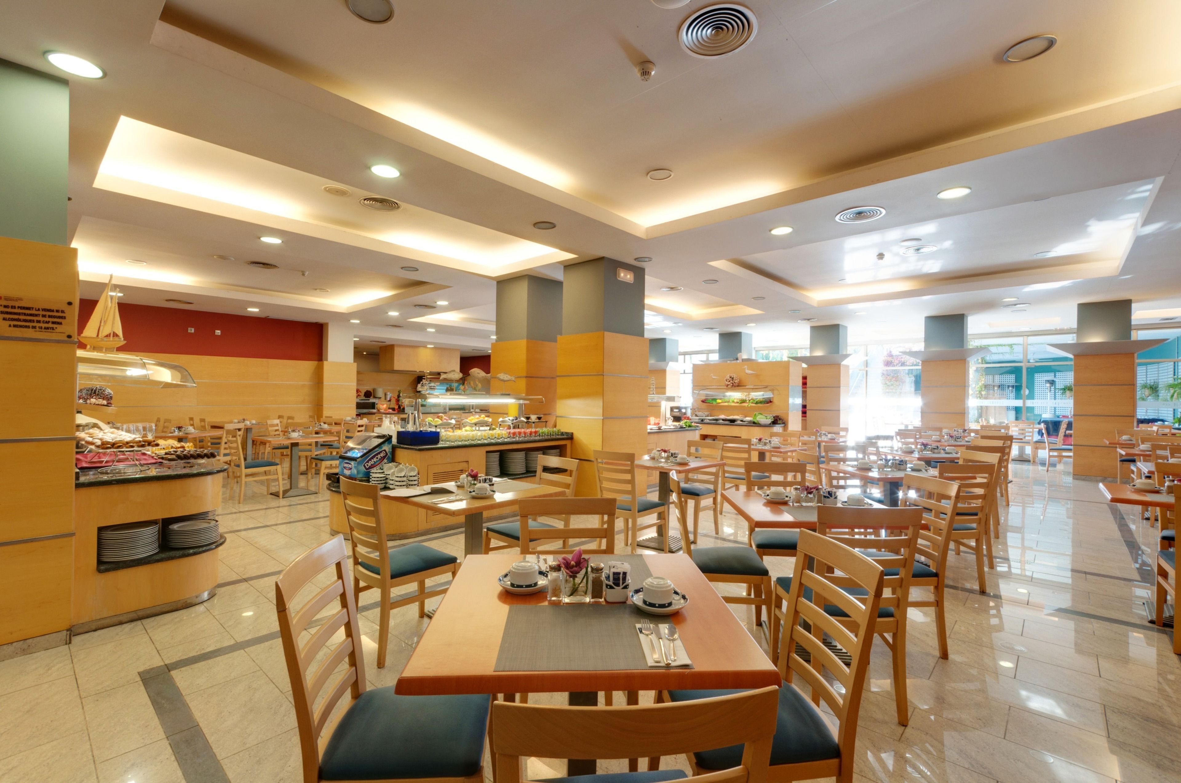 A spacious dining area with multiple tables and chairs, a buffet counter, and a kitchen in the background.