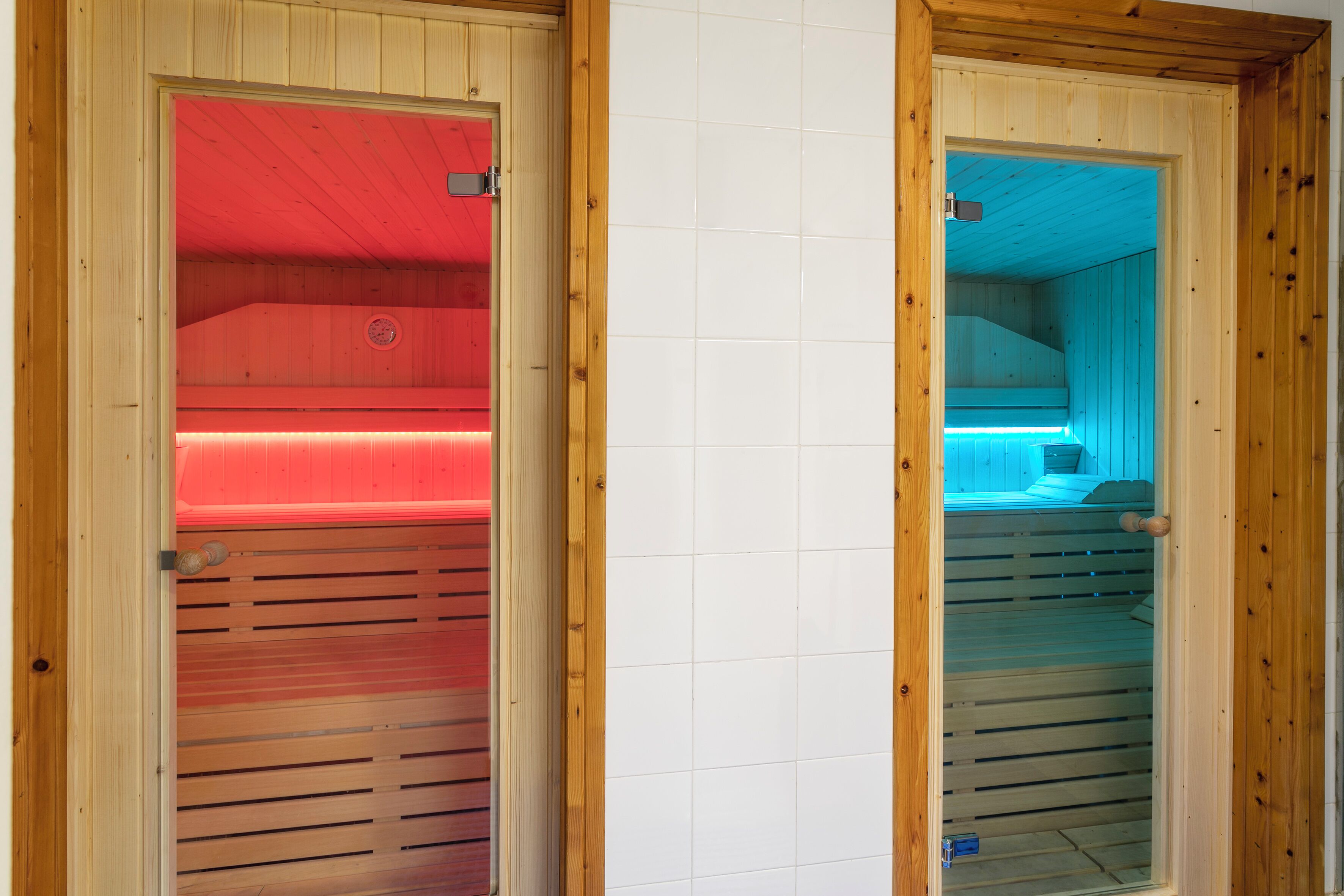 Deux salles de sauna dotées de portes en bois, l’une éclairée en rouge et l’autre en bleu.
