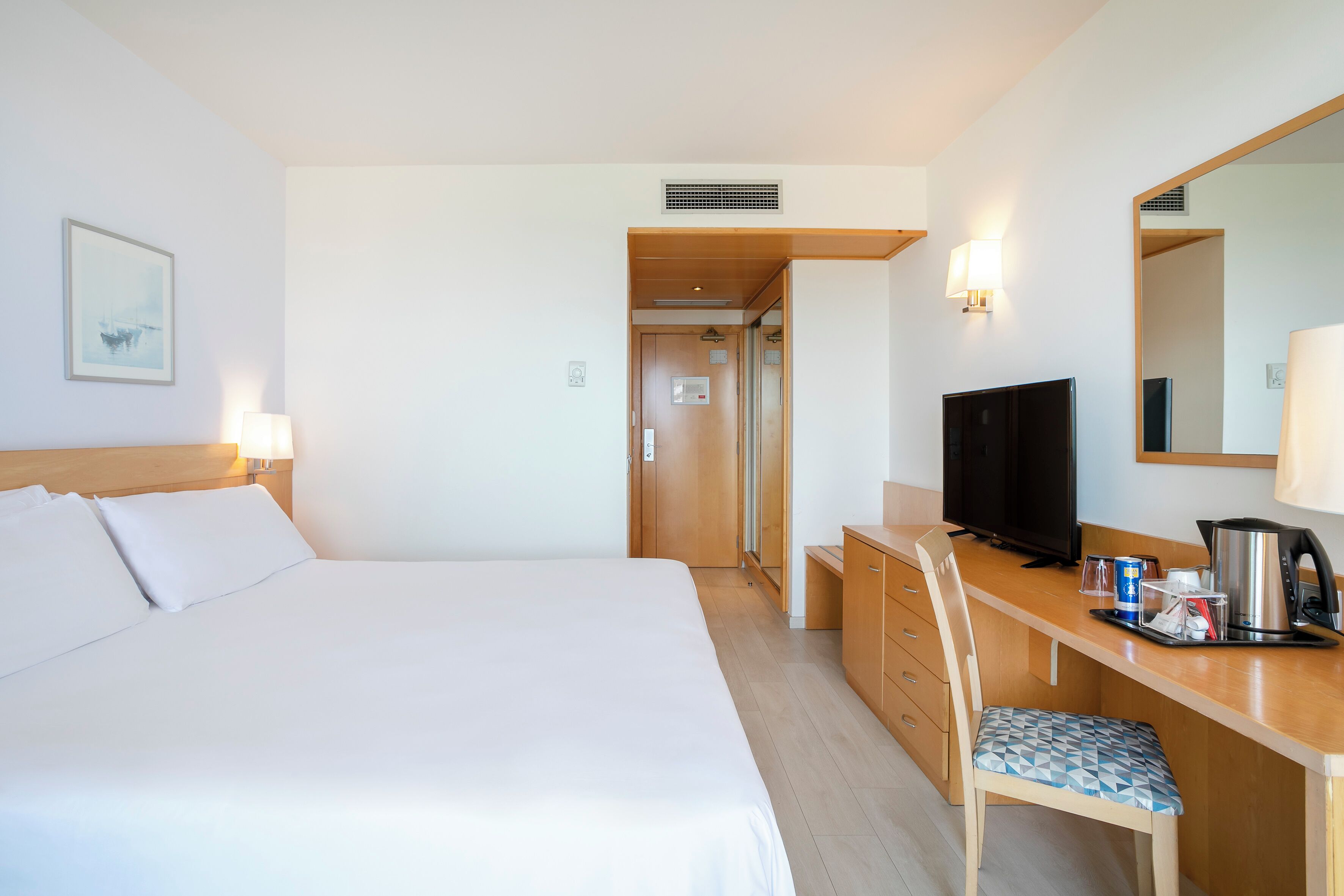 A hotel room with a large bed, a desk with a television, a chair, and a coffee maker.