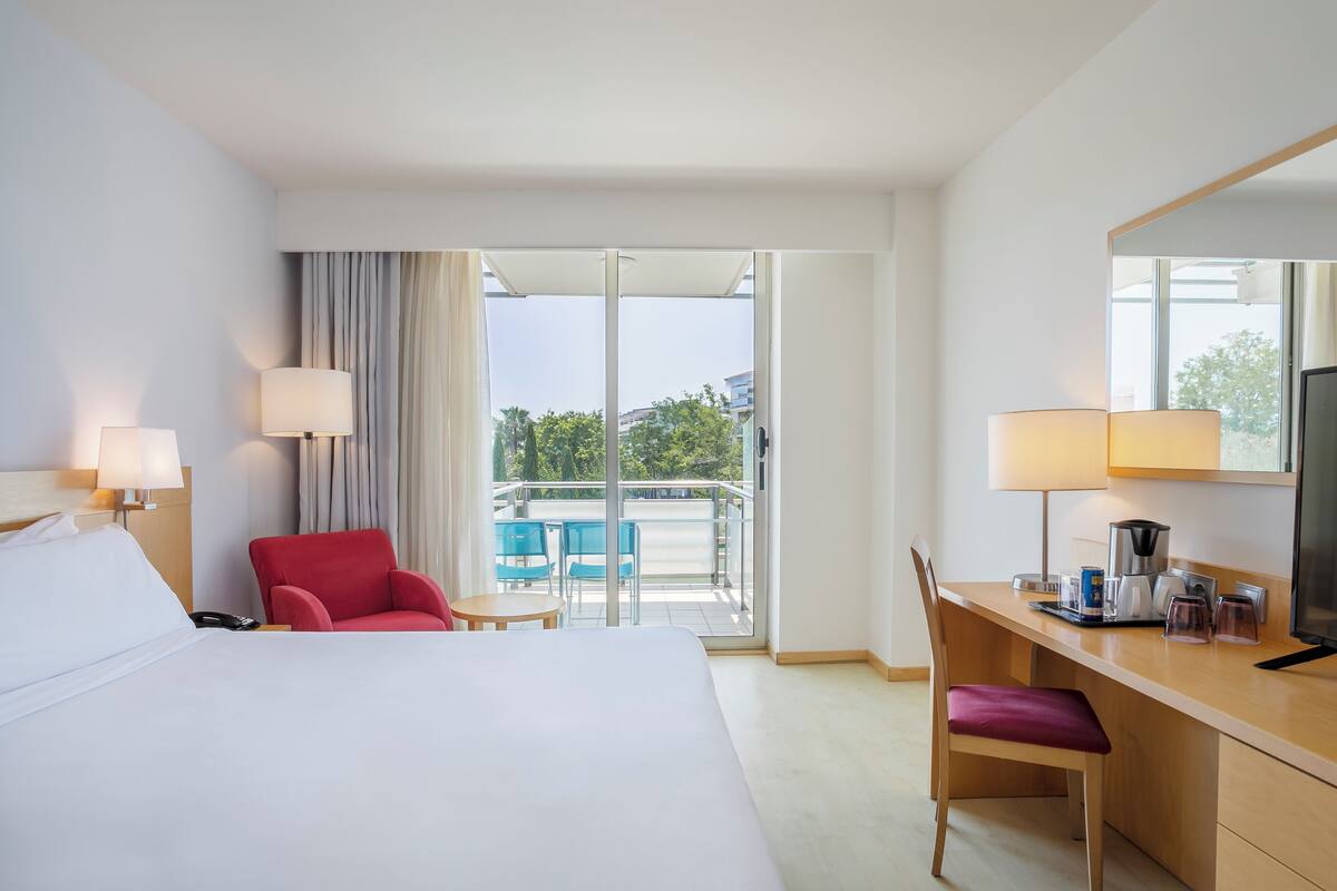 Une chambre d’hôtel comprenant un lit, un bureau avec une chaise, une télévision et un balcon avec des chaises.