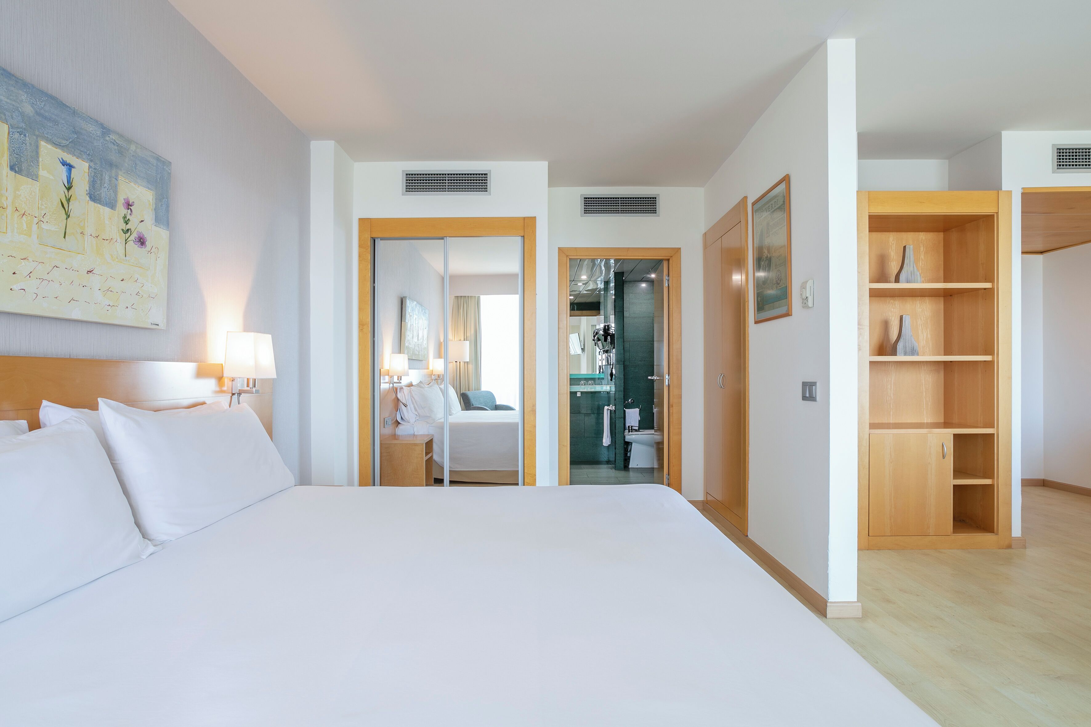 Une chambre d’hôtel avec un grand lit, une table de chevet, une lampe, un tableau au mur et une armoire en bois.