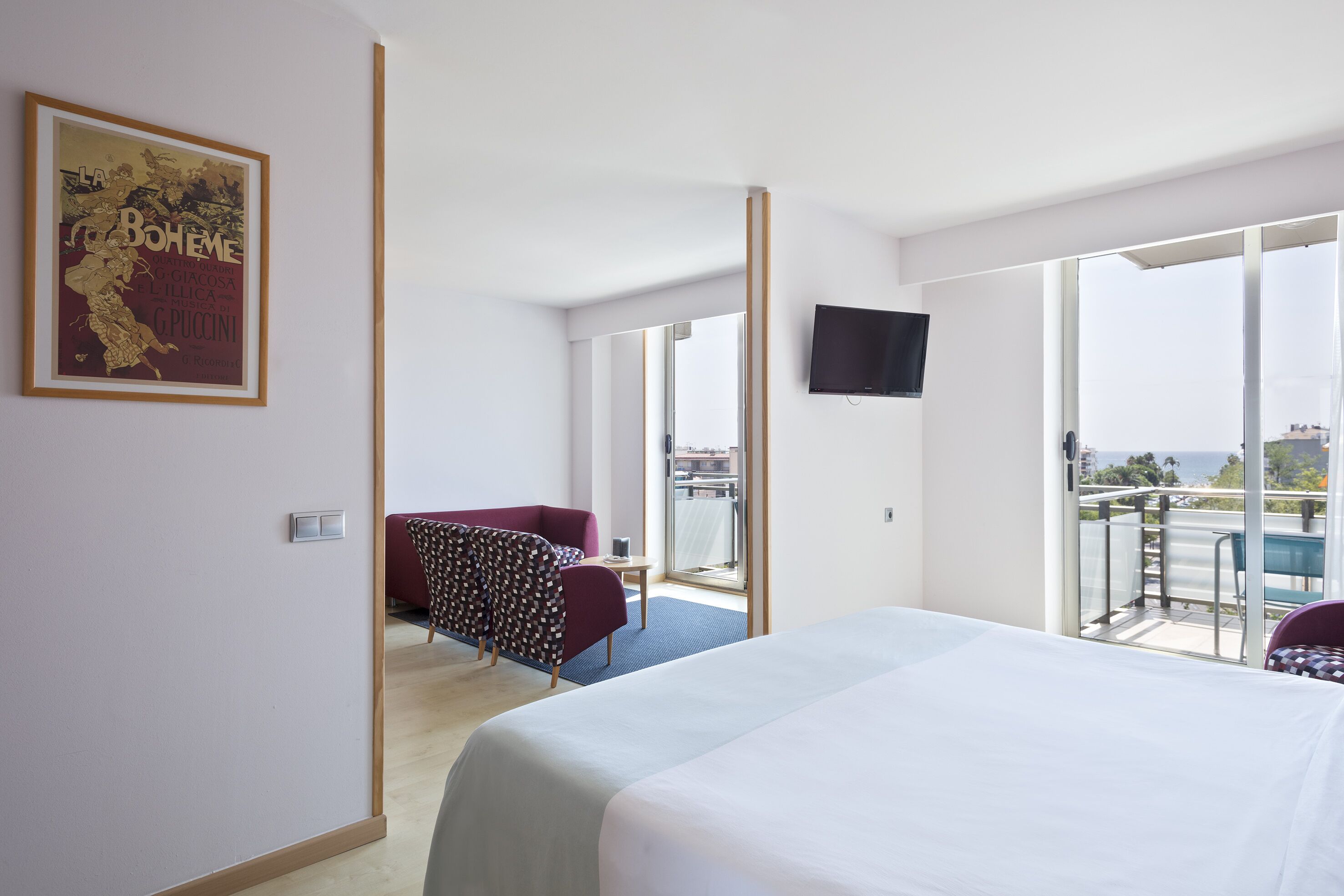A hotel room with a bed, a chair, a TV, and a balcony with a view.