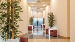 A modern lobby with a polished floor, red seating, and tall bamboo plants. - Sol Port Cambrils (Cambrils)