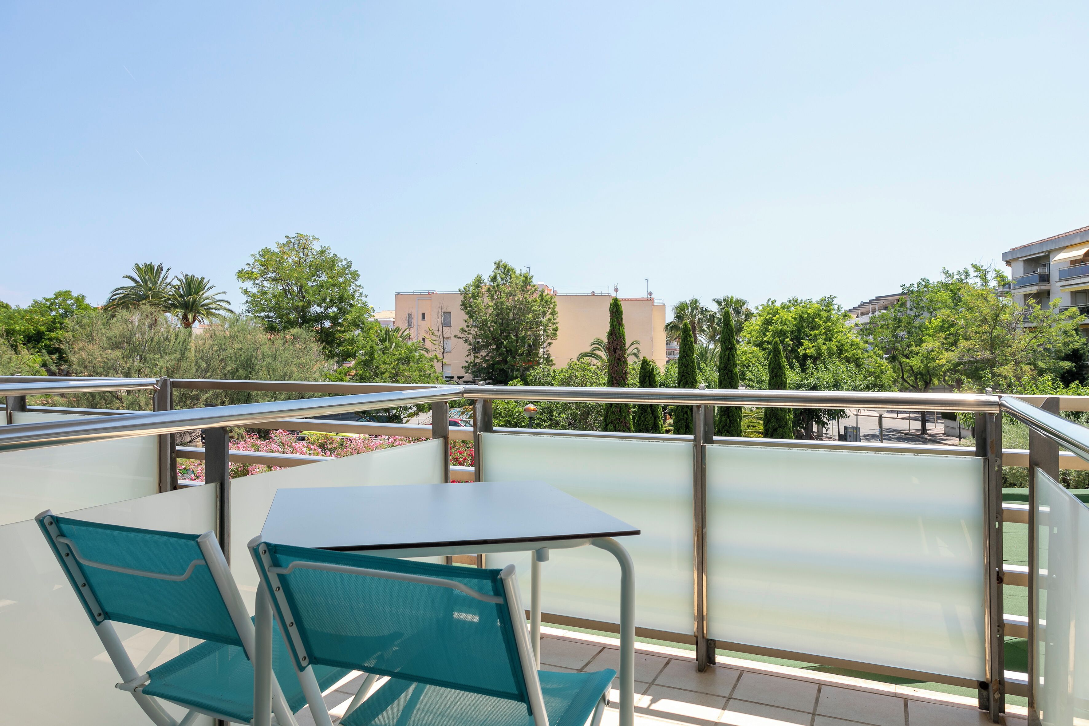 Un balcon avec une table et des chaises, une vue sur les bâtiments et les arbres, et un ciel dégagé.