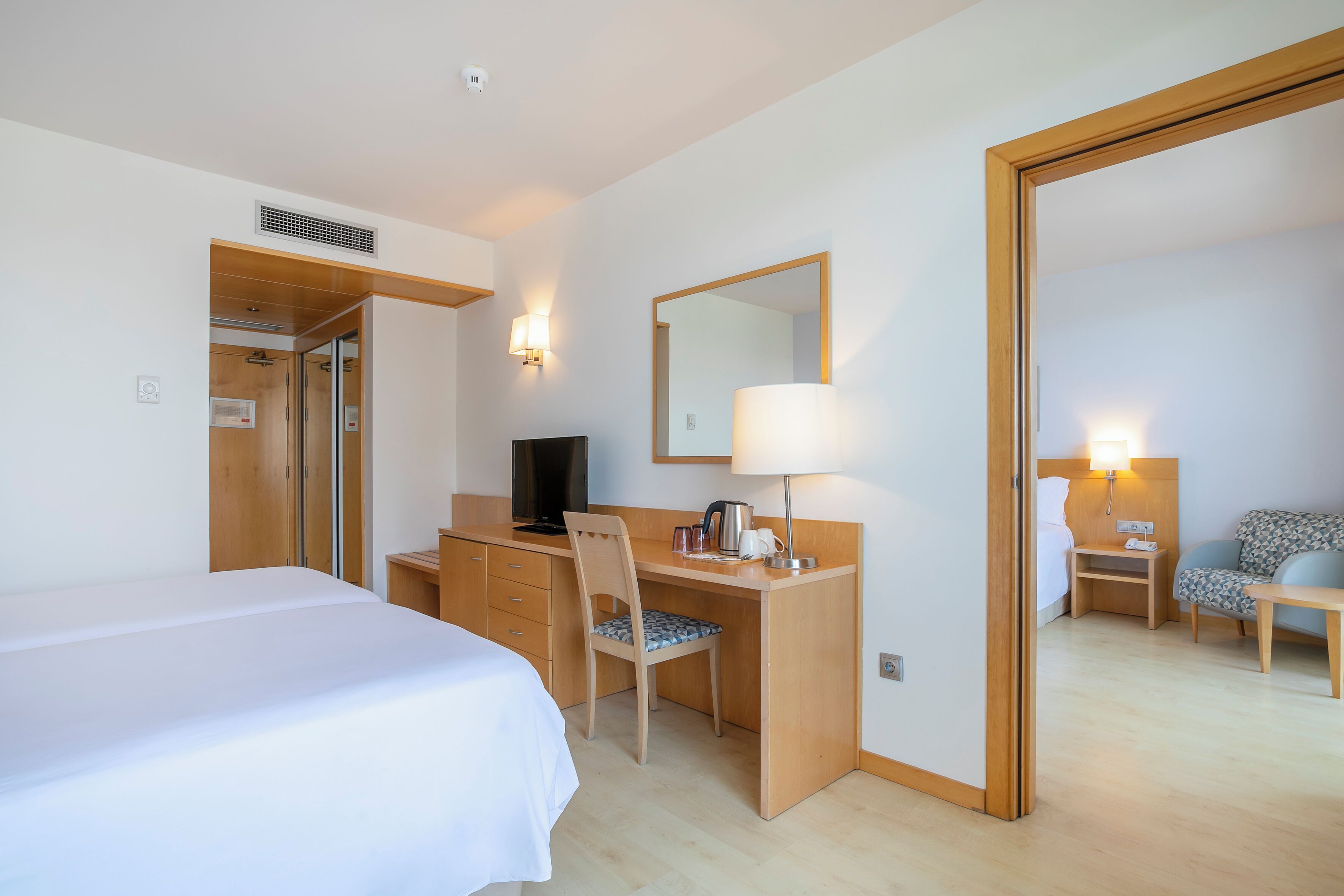 Una camera d'albergo con un letto, una scrivania con sedia, una televisione, una lampada e uno specchio.