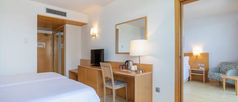 Quarto de hotel com cama, secretária, cadeira, televisão, candeeiro e espelho.