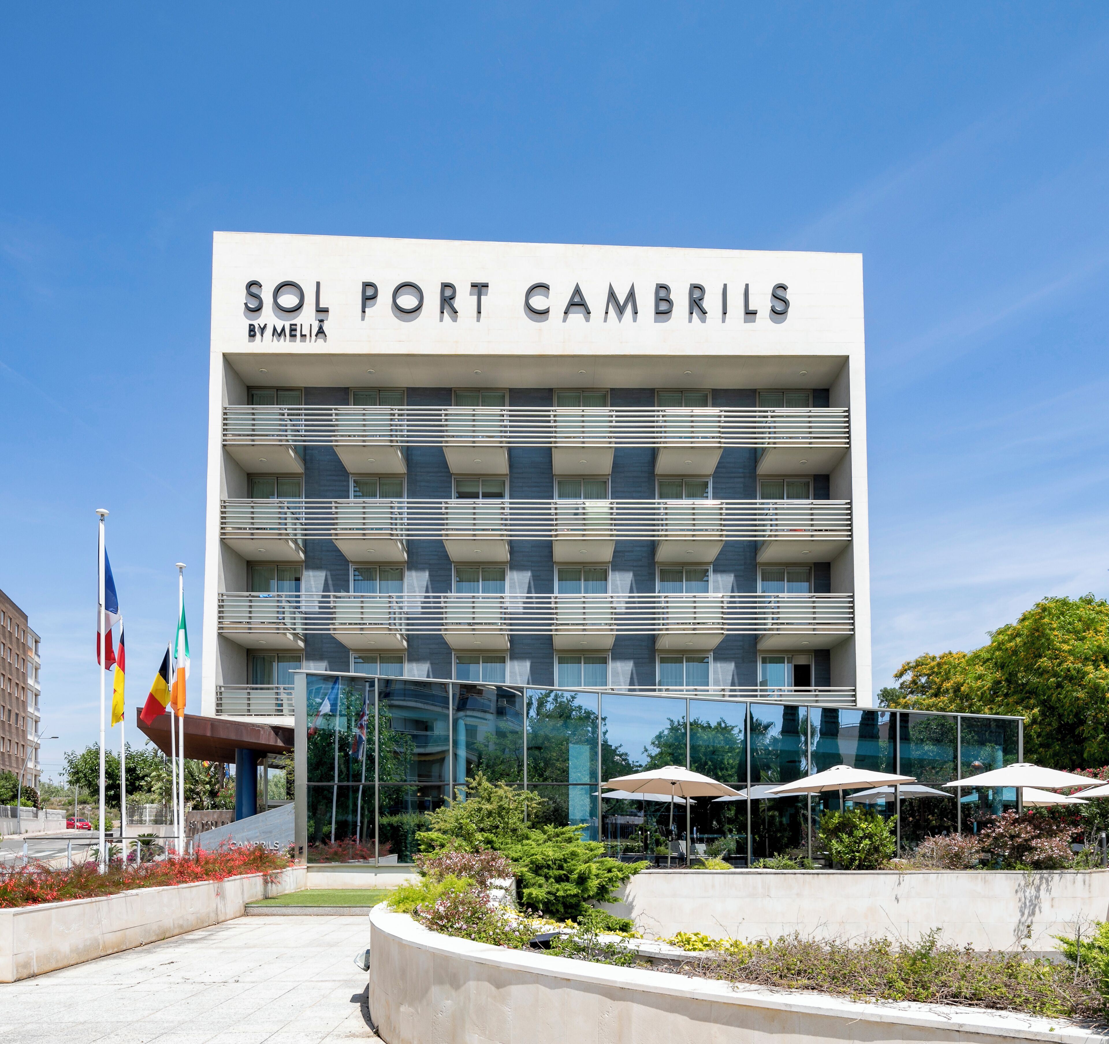 A modern hotel building named 'Sol Port Cambrils' with a glass facade, multiple balconies, and a landscaped entrance area.