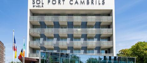A modern hotel building named 'Sol Port Cambrils' with a glass facade, multiple balconies, and a landscaped entrance area.