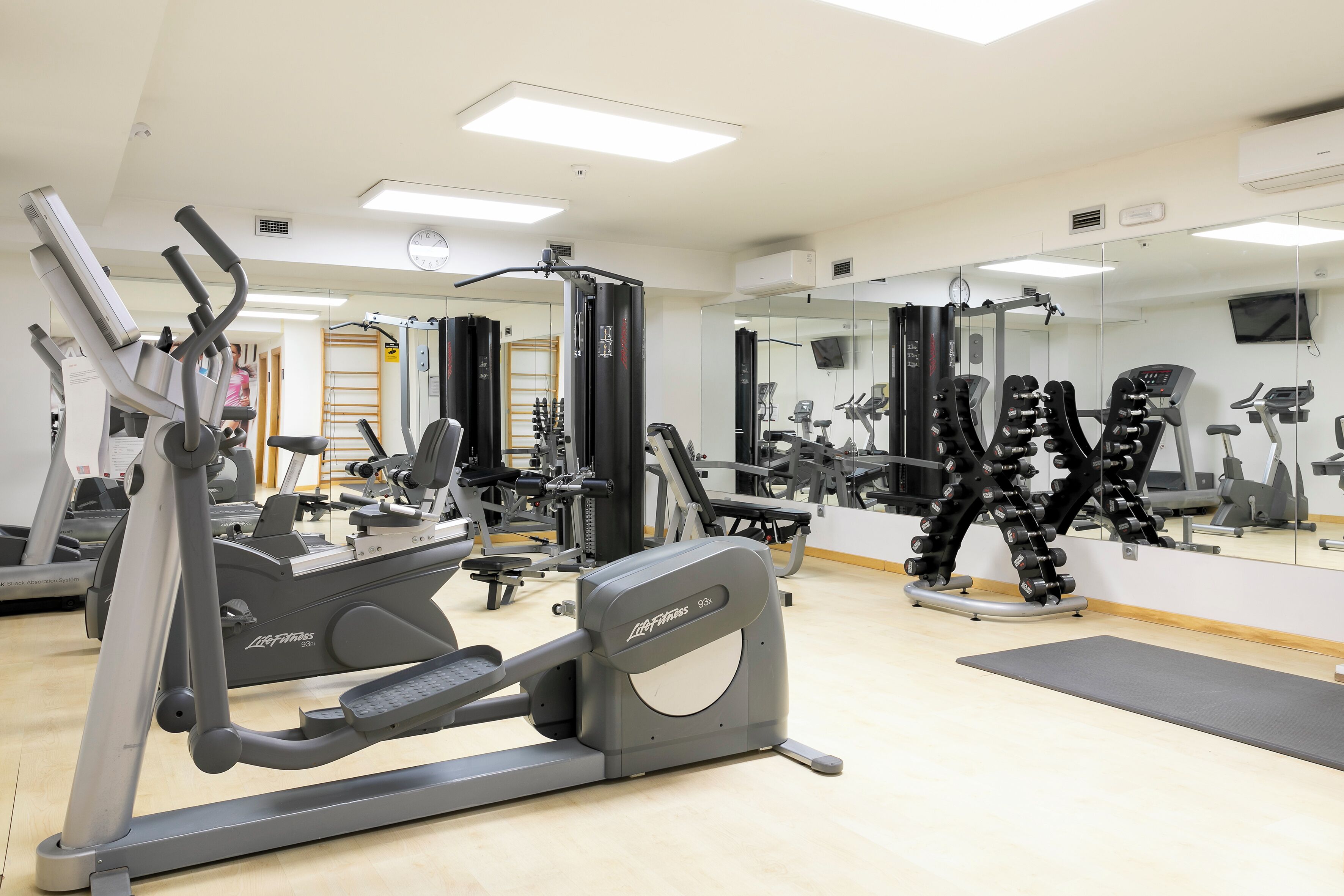 Ein Fitnessstudio mit Cardiogeräten, Gewichten und einem großen Spiegel.