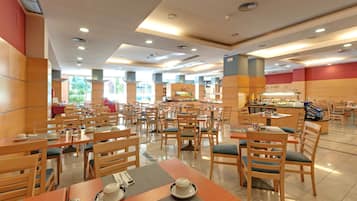Un amplio comedor con varias mesas y sillas, una barra de buffet y vistas al exterior.