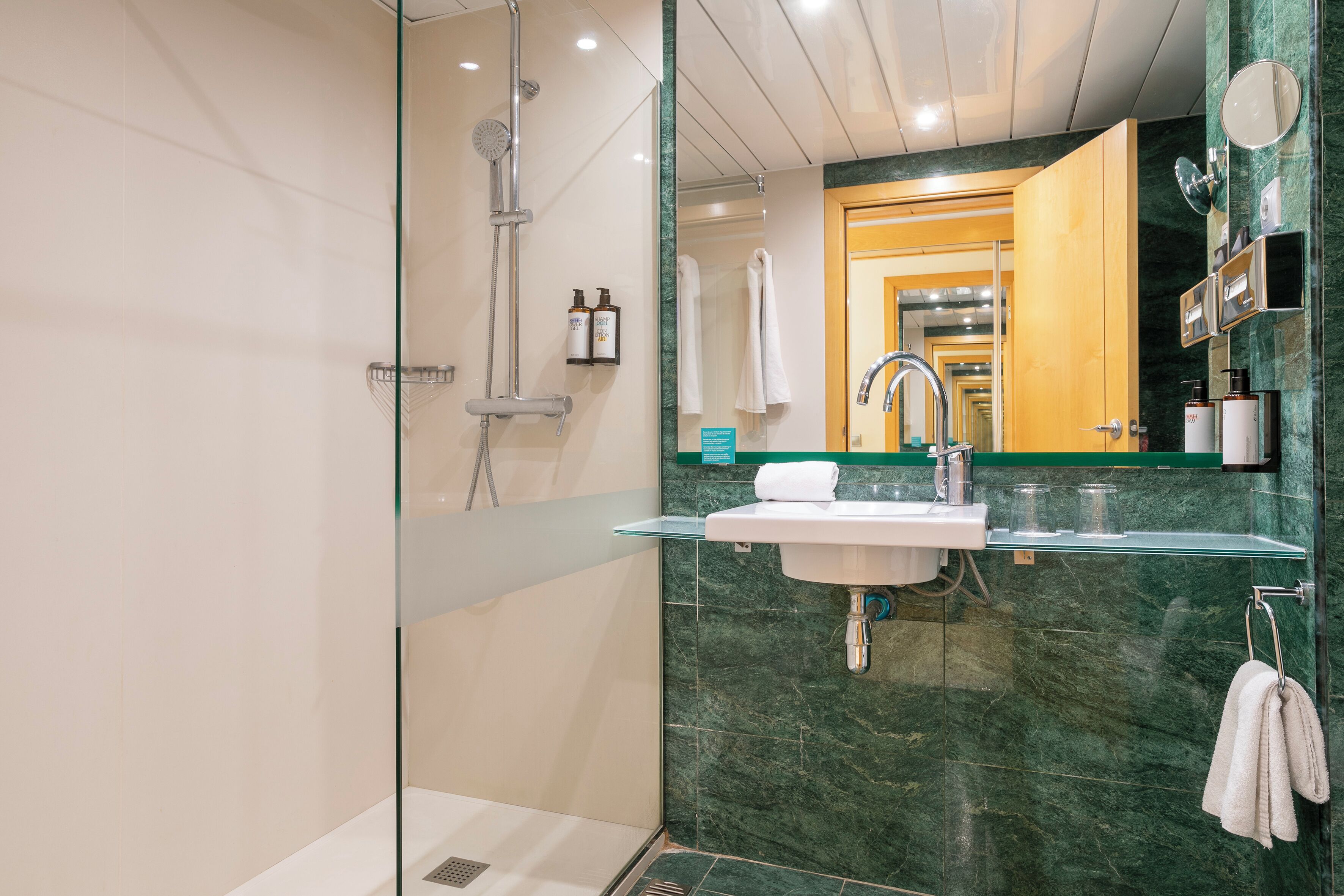 Un baño moderno con cabina de ducha de vidrio, lavabo con encimera de mármol y espejo sobre el lavabo.