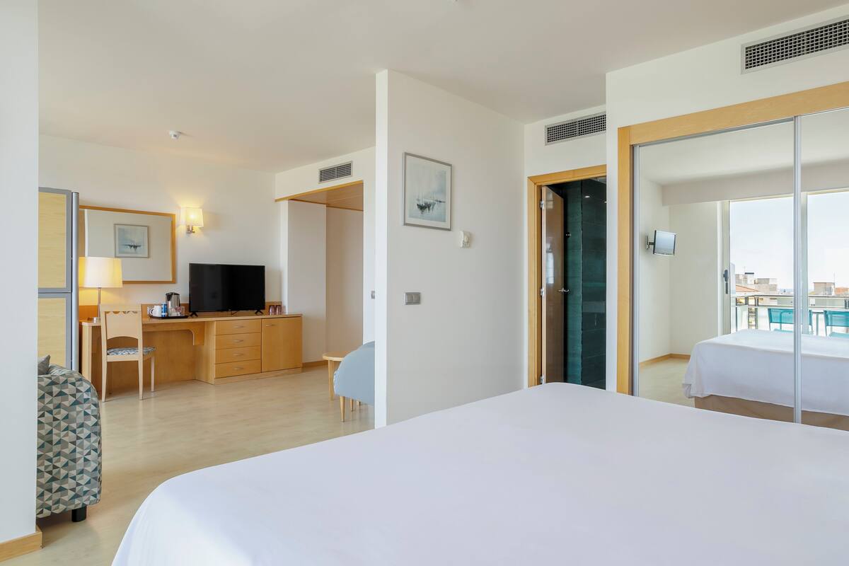 Une chambre d’hôtel avec un grand lit, un bureau avec une chaise, une télévision et une vue sur la ville, visible à travers une porte vitrée.