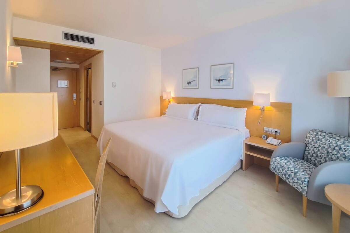 Une chambre d’hôtel avec un grand lit, des tables de chevet avec des lampes, un bureau et une chaise.