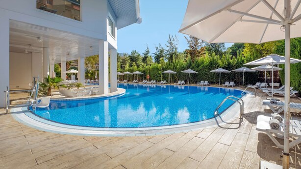 A swimming pool with lounge chairs and umbrellas, surrounded by a covered area with a building in the background. - Ponient Pirámide Salou by PortAventura World (Salou)