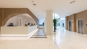A modern hotel lobby with a reception desk, a staircase, and a view of the outside. - Ponient Pirámide Salou by PortAventura World (Salou)