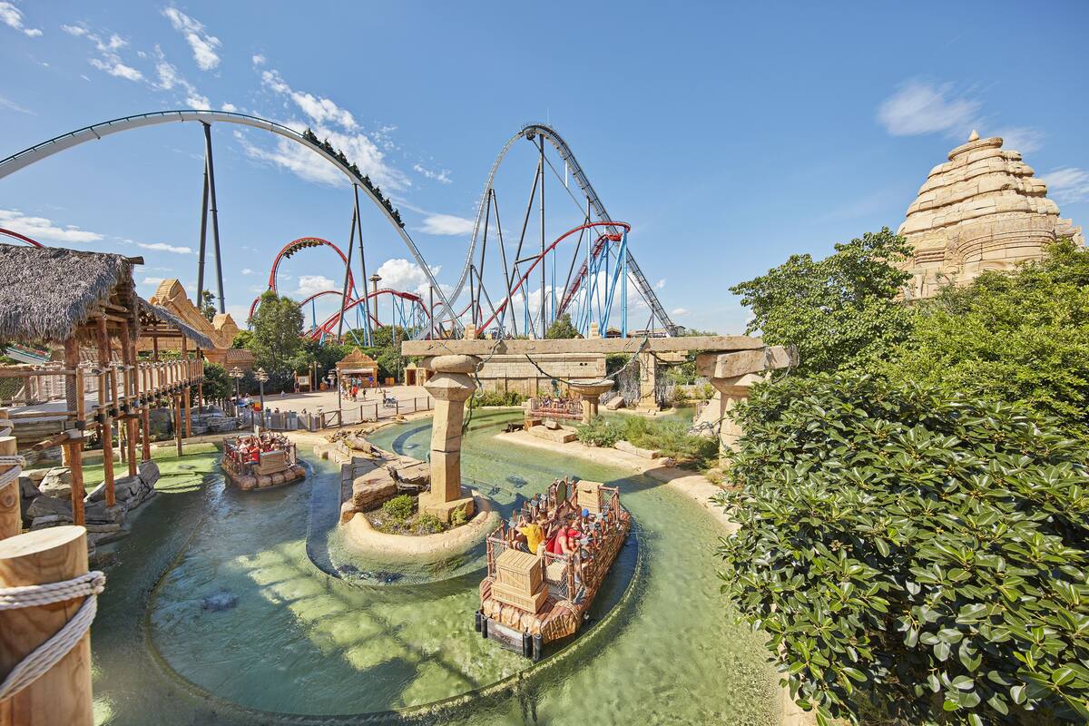 A theme park with roller coasters, a river with boats, and traditional architecture.