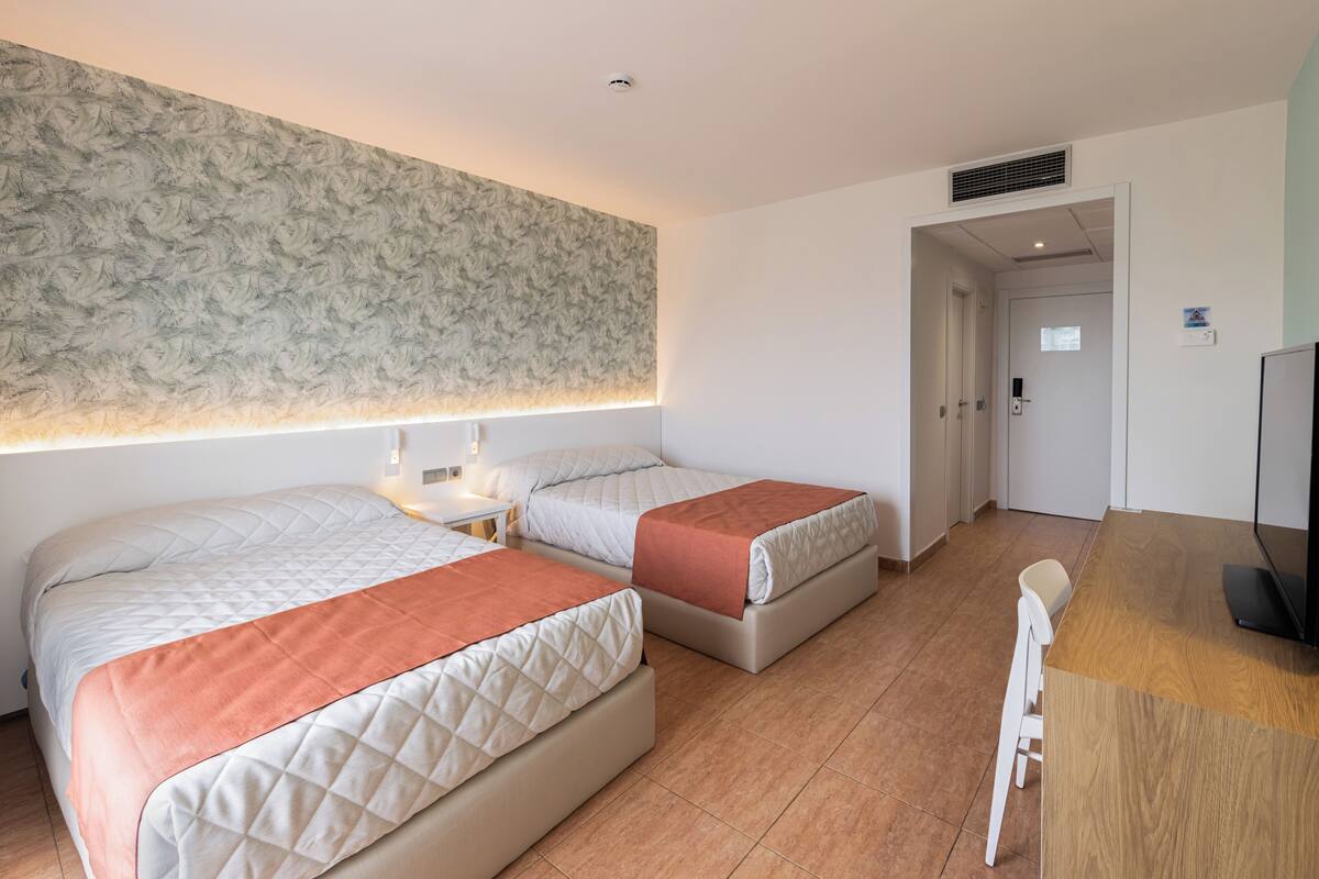 A hotel room with two beds, a desk, and a television.