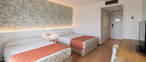 A hotel room with two beds, a desk, and a television.