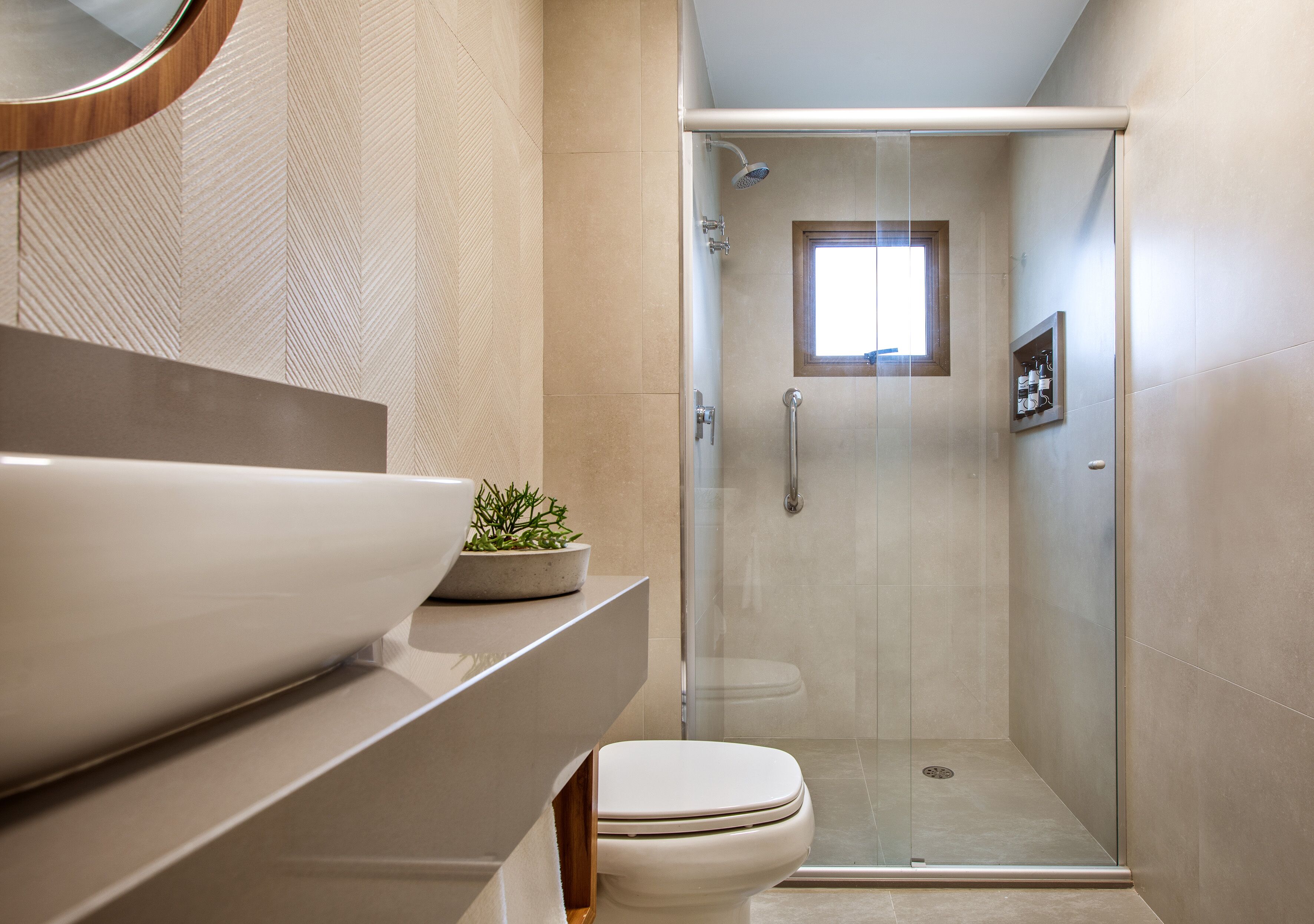 Un baño moderno con ducha de vidrio, un lavamanos grande de color blanco y una planta en maceta sobre la encimera.