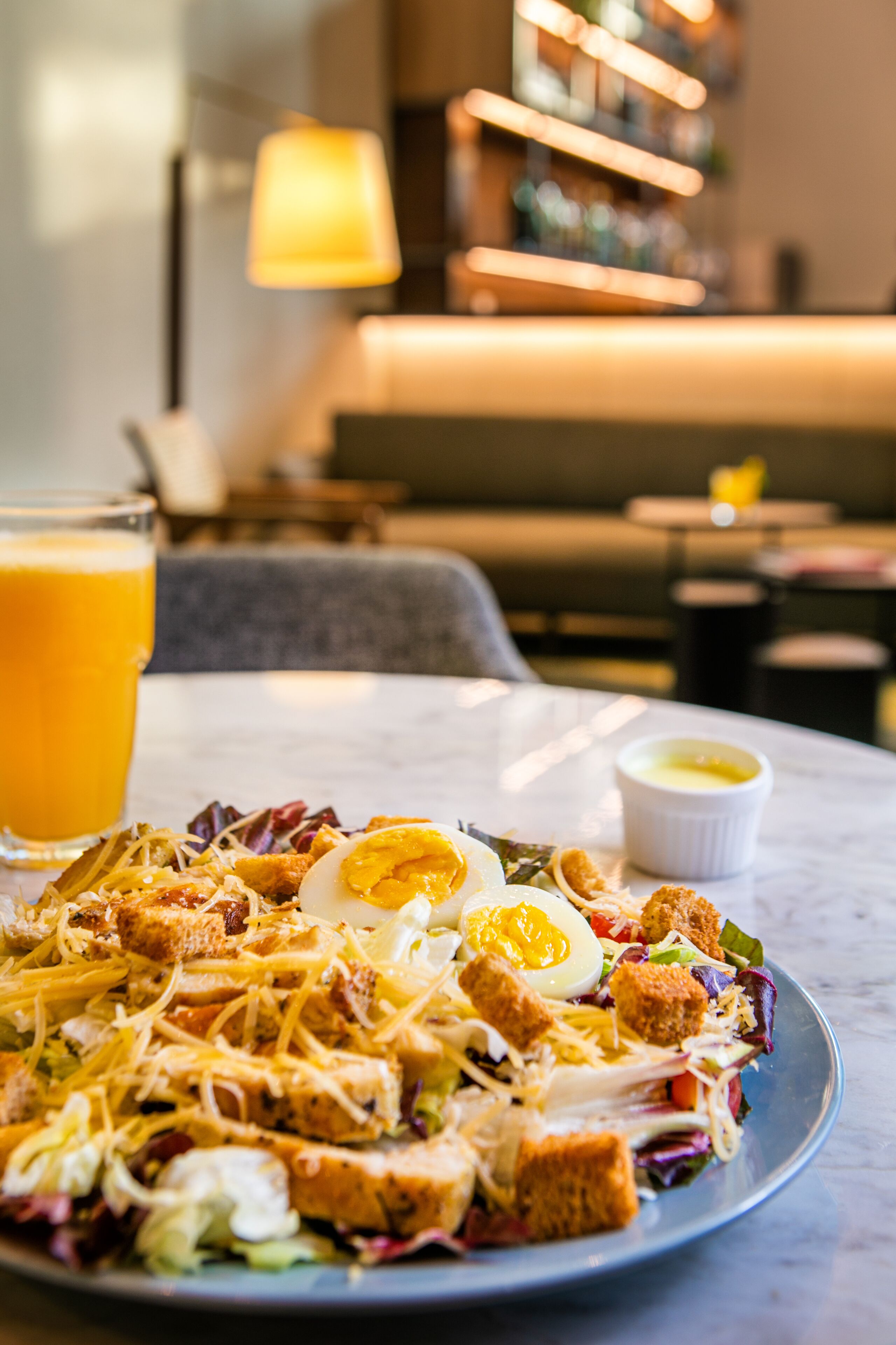 A plate of salad with croutons and a boiled egg on a marble table in a restaurant setting.