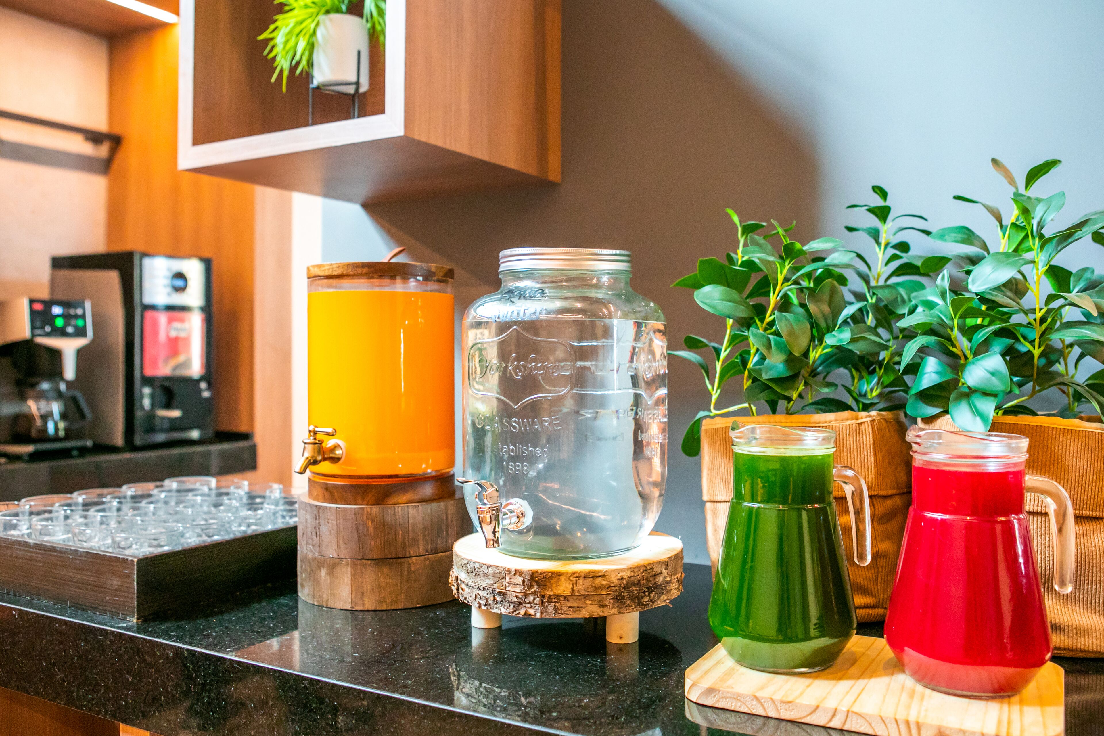 Un comptoir de cuisine avec une machine à café, un bocal en verre et deux carafes contenant des boissons vertes et rouges.