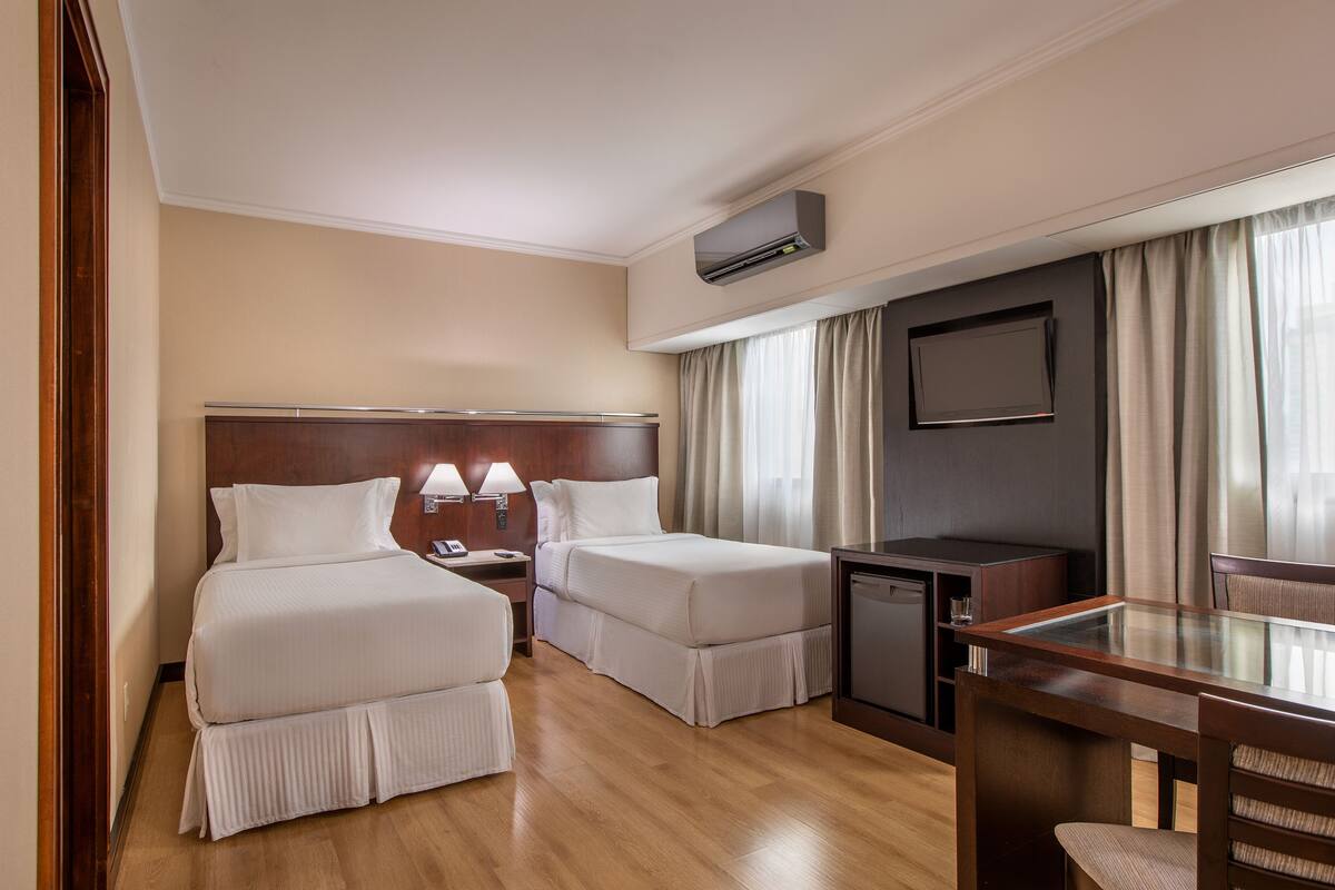 A hotel room with two beds, a desk, a television, and a minibar.