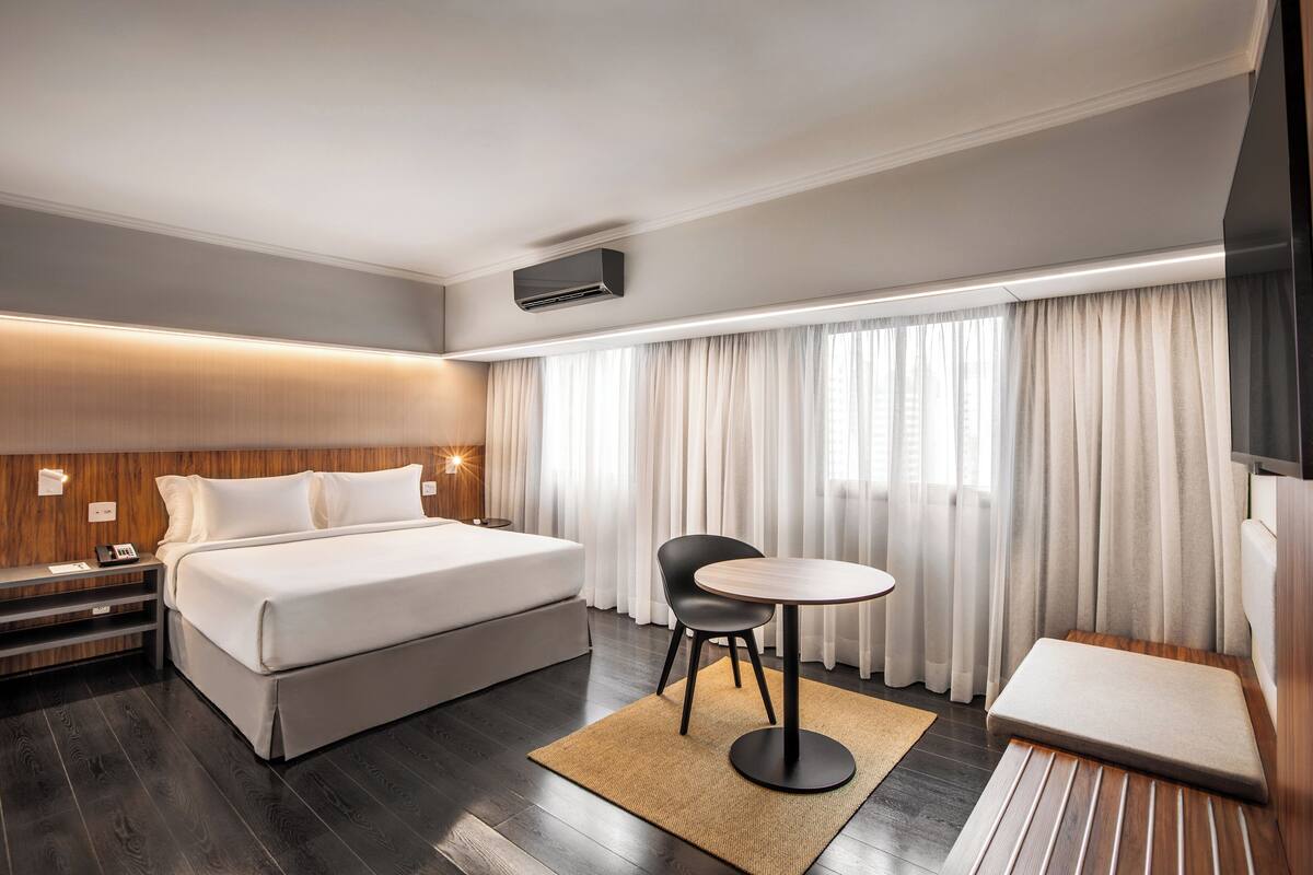 A modern hotel room with a large bed, a small round table, a chair, a sofa, and a TV.
