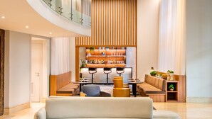 Un vestíbulo amplio con diseño moderno, que presenta una zona de estar curvilínea, un bar y un techo de madera con iluminación lineal.