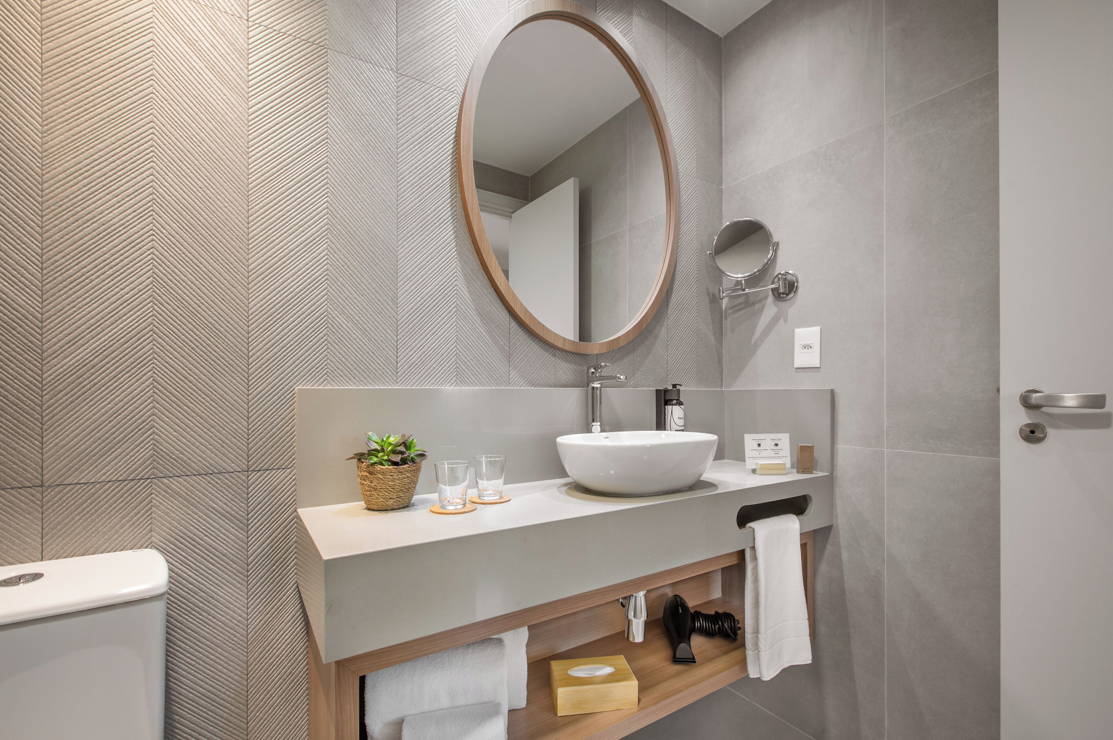 A modern bathroom with a large oval mirror, a vessel sink, and a wooden vanity.